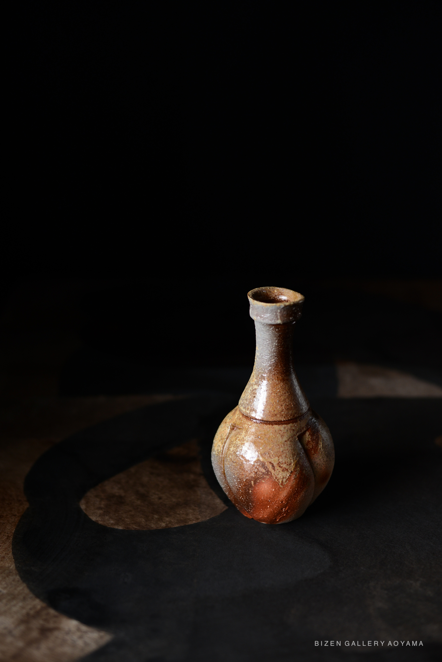 A Bizen pottery Tokkuri, featuring a unique shape with earthy tones and a glossy finish, set against a dark background.