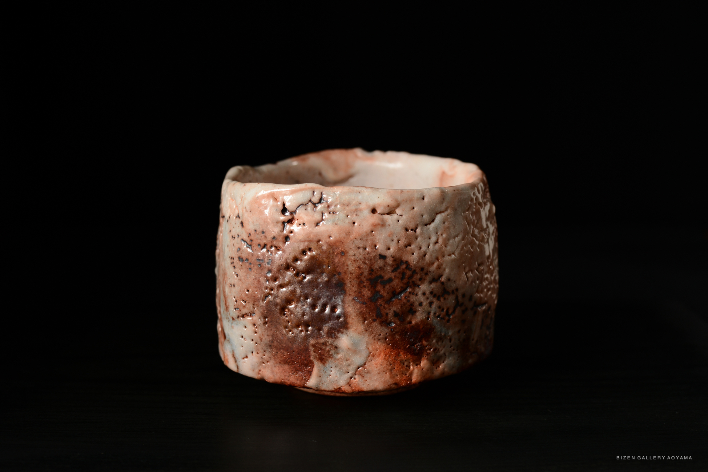 Shino Chawan ceramic bowl with textured surface in earthy tones, set against a black background.