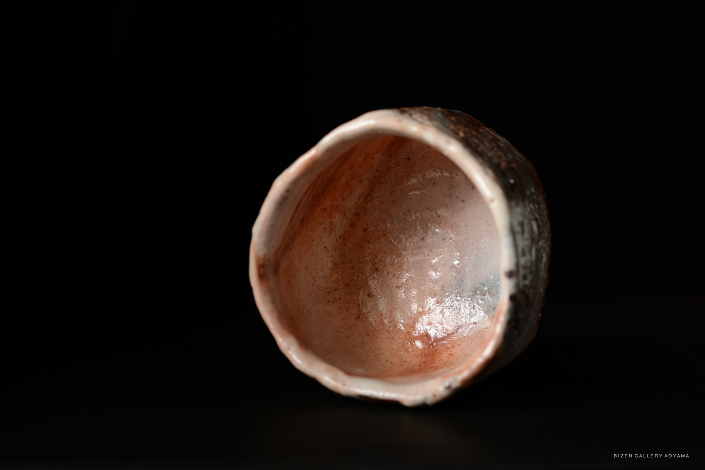 An interior view of a Shino Chawan tea bowl, showcasing its smooth, earthy ceramic texture and warm color tones against a black background.