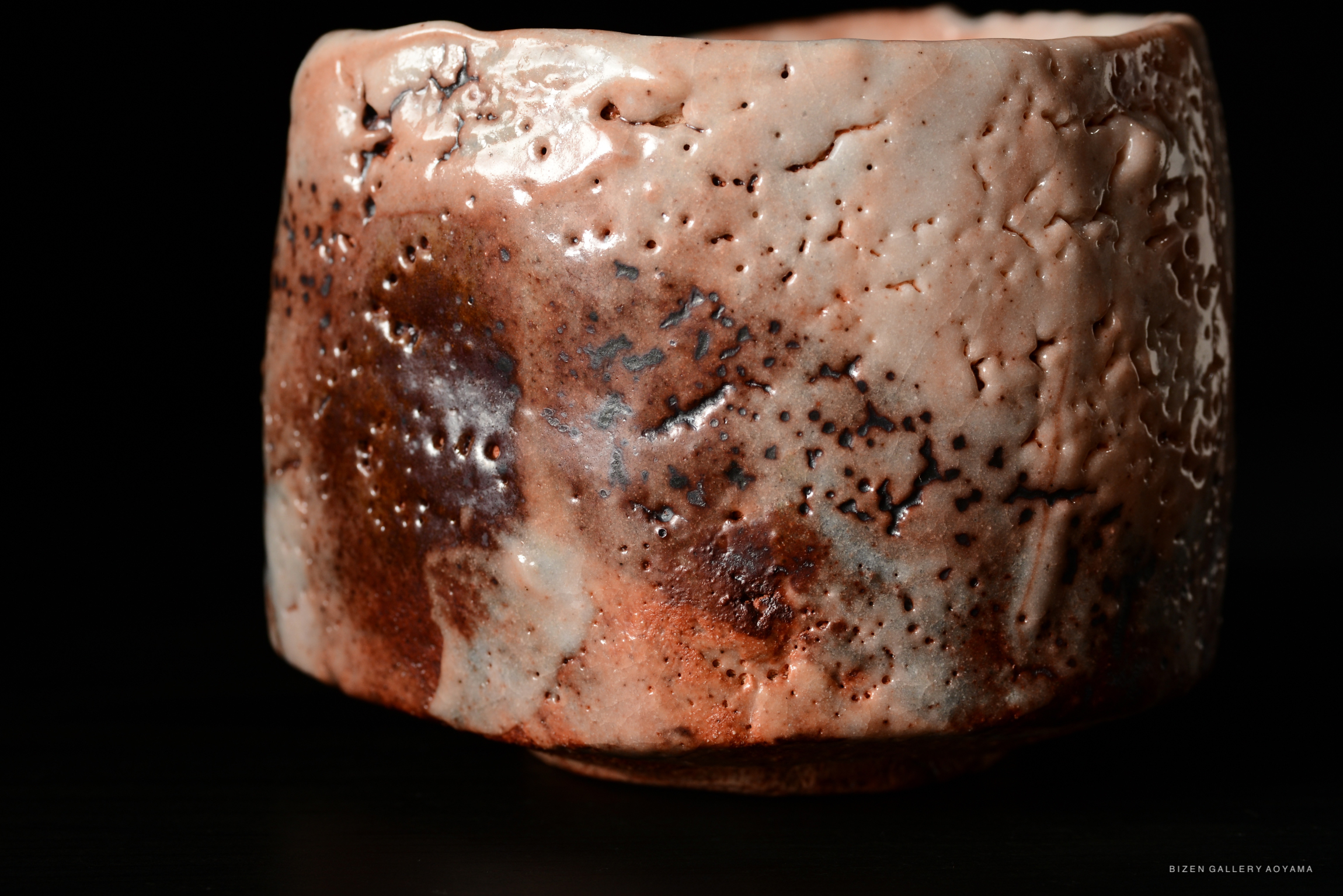 Close-up of a Shino Chawan tea bowl featuring a textured and speckled surface with shades of brown and cream, set against a black background.