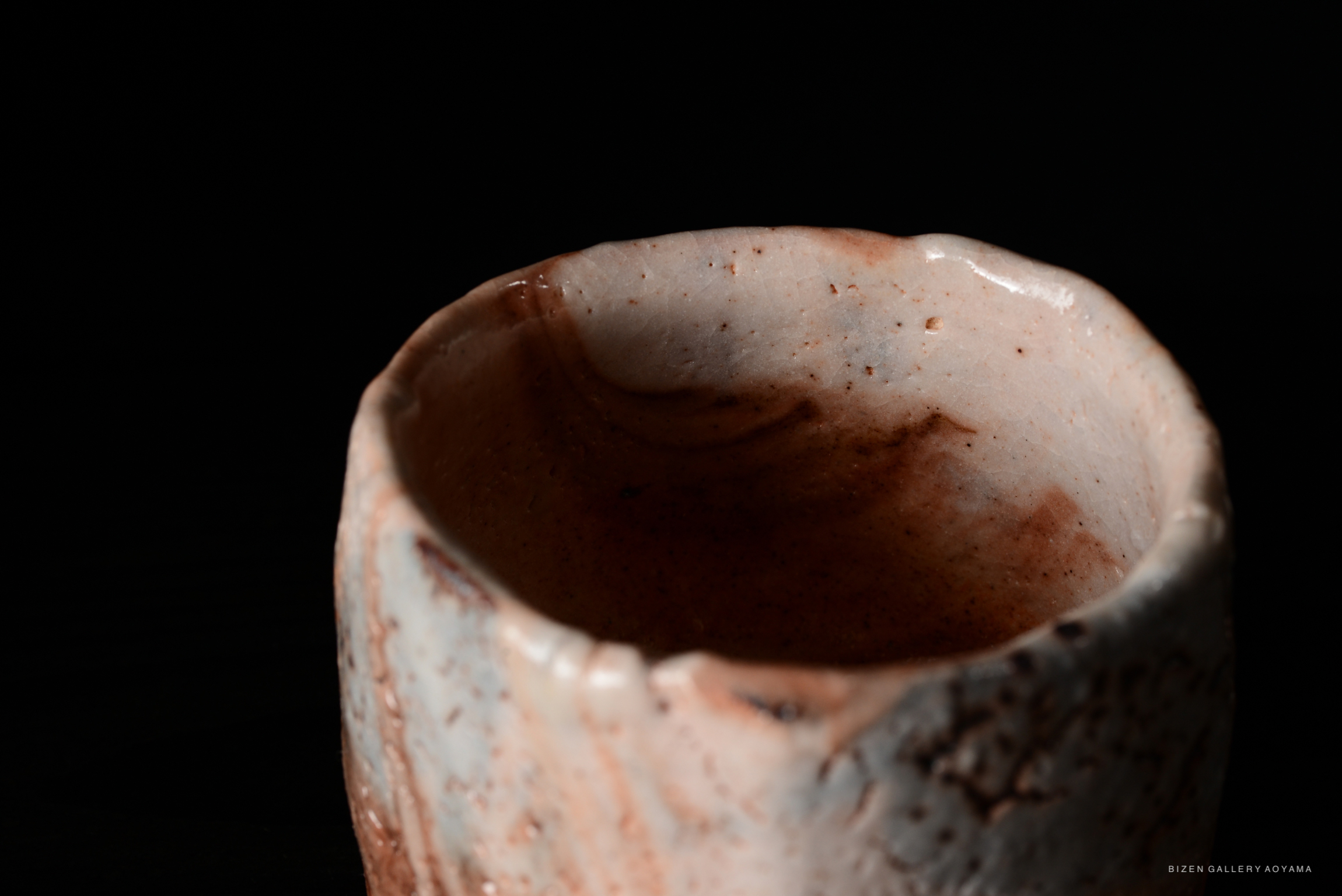 Close-up view of a shino chawan, a traditional Japanese tea bowl, showcasing its unique glaze and texture against a dark background.