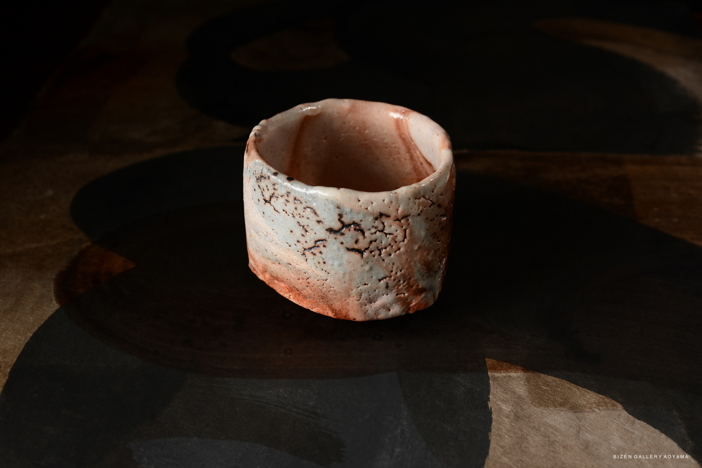 A beautifully crafted Shino chawan tea bowl with a rustic design, featuring soft pastel hues and textured details, displayed against a dark background.
