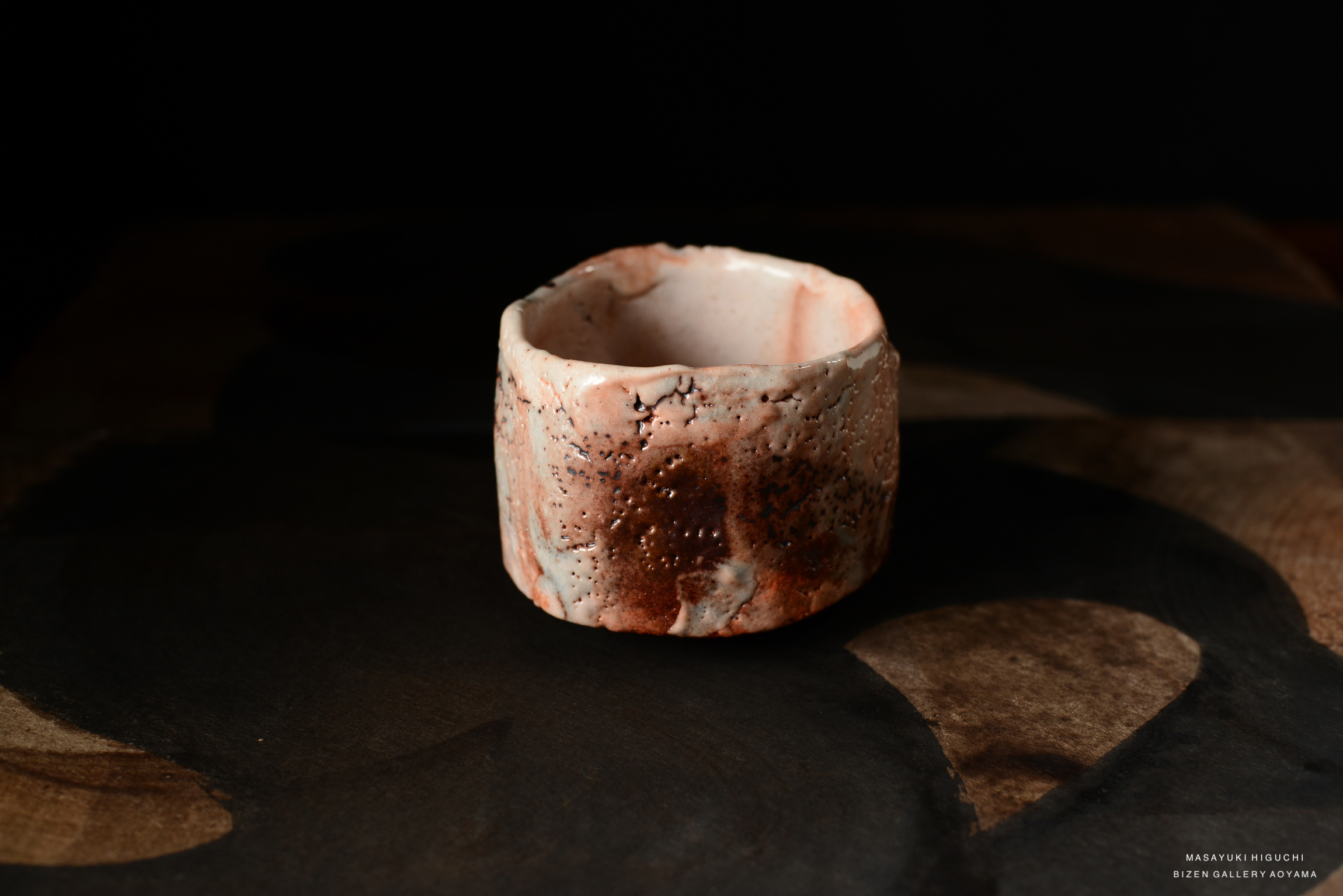 Close-up of a Shino Chawan tea bowl with a textured surface in earthy colors, placed on a dark wooden surface.