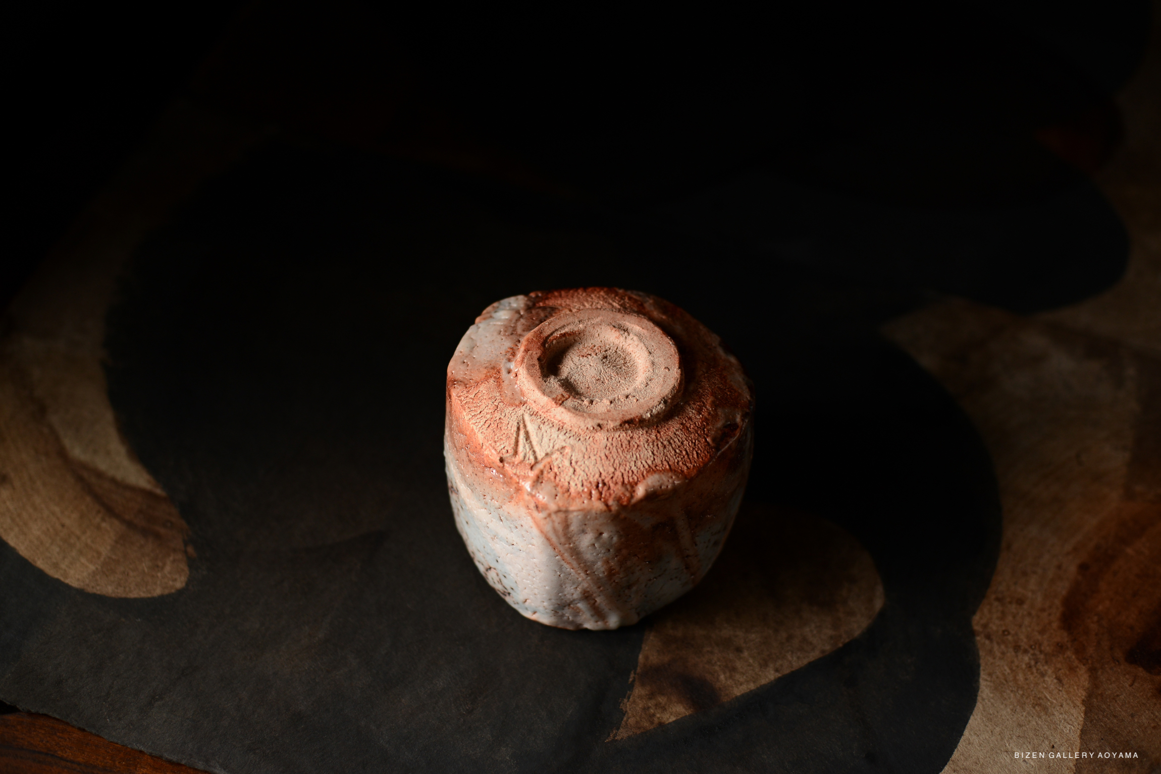 A close-up view of a Shino chawan (tea bowl) with a reddish-brown and white glaze, resting on a dark surface.