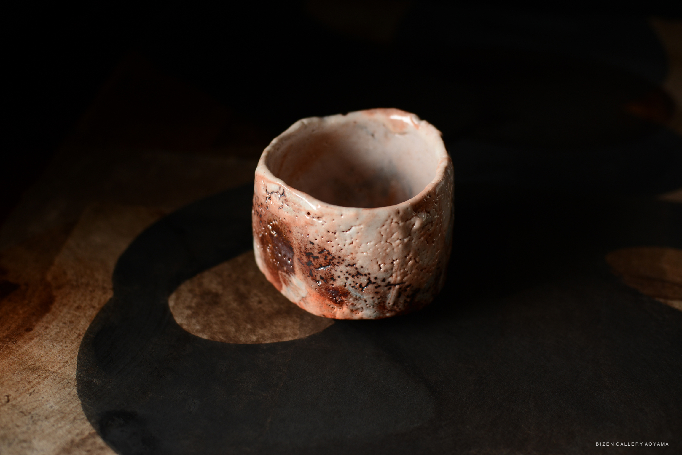 A close-up view of a Shino Chawan tea bowl, showcasing its textured surface and earthy colors, placed on a dark background.