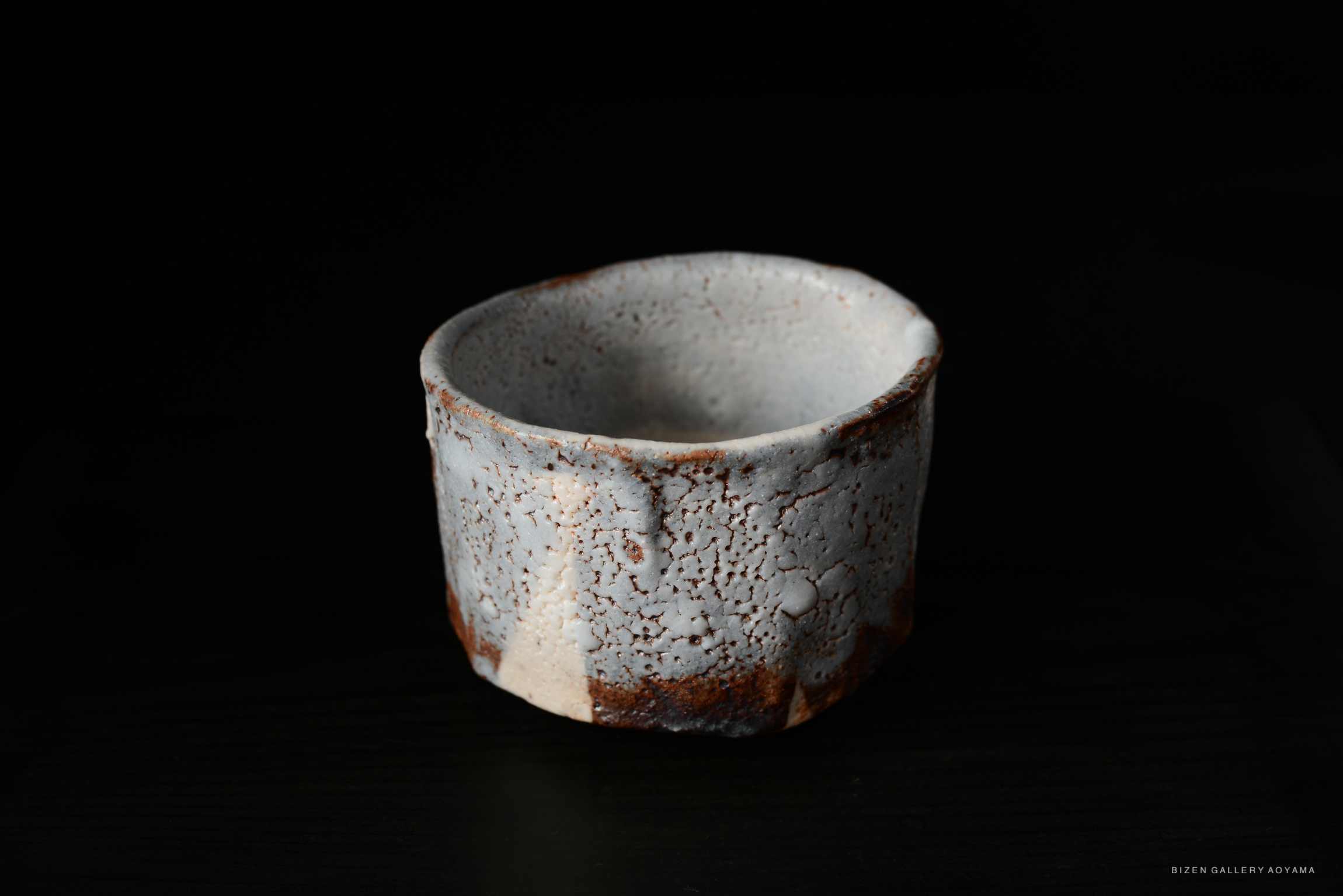 A handcrafted Shino Chawan tea bowl featuring a textured surface with cracks and earthy tones, showcased against a dark background.
