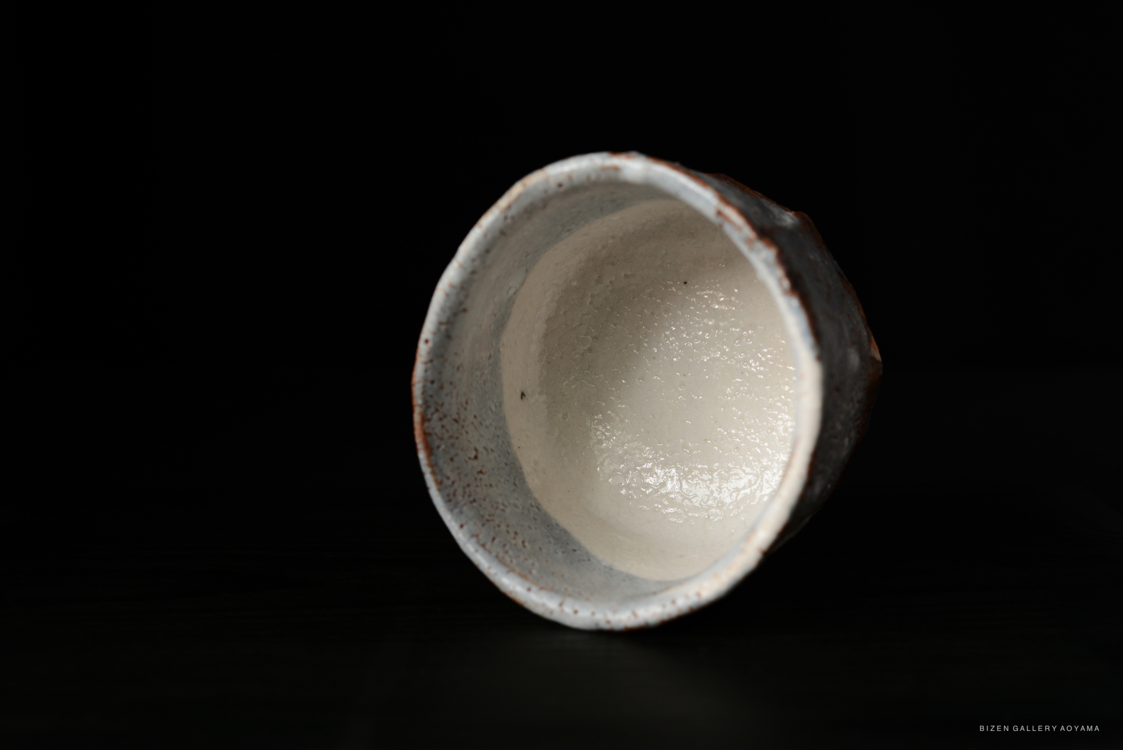 Interior view of a Shino Chawan tea bowl, featuring a smooth white glaze and textured rim, displayed against a dark background.
