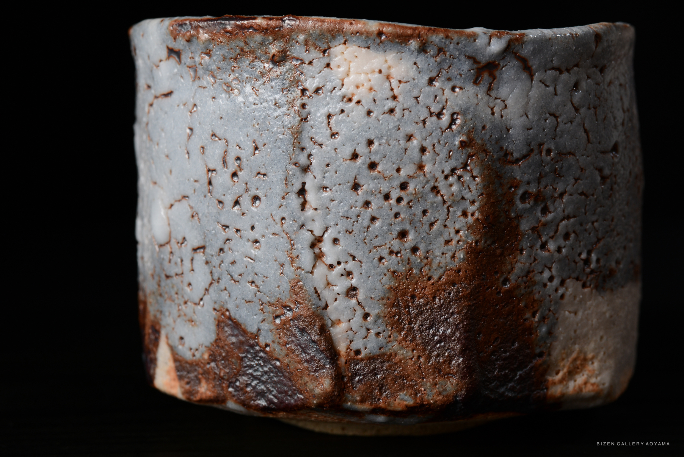 Close-up view of a Nezumi Shino tea bowl showcasing its pale blue-grey color and textured surface, with visible glaze variations and rust marks.