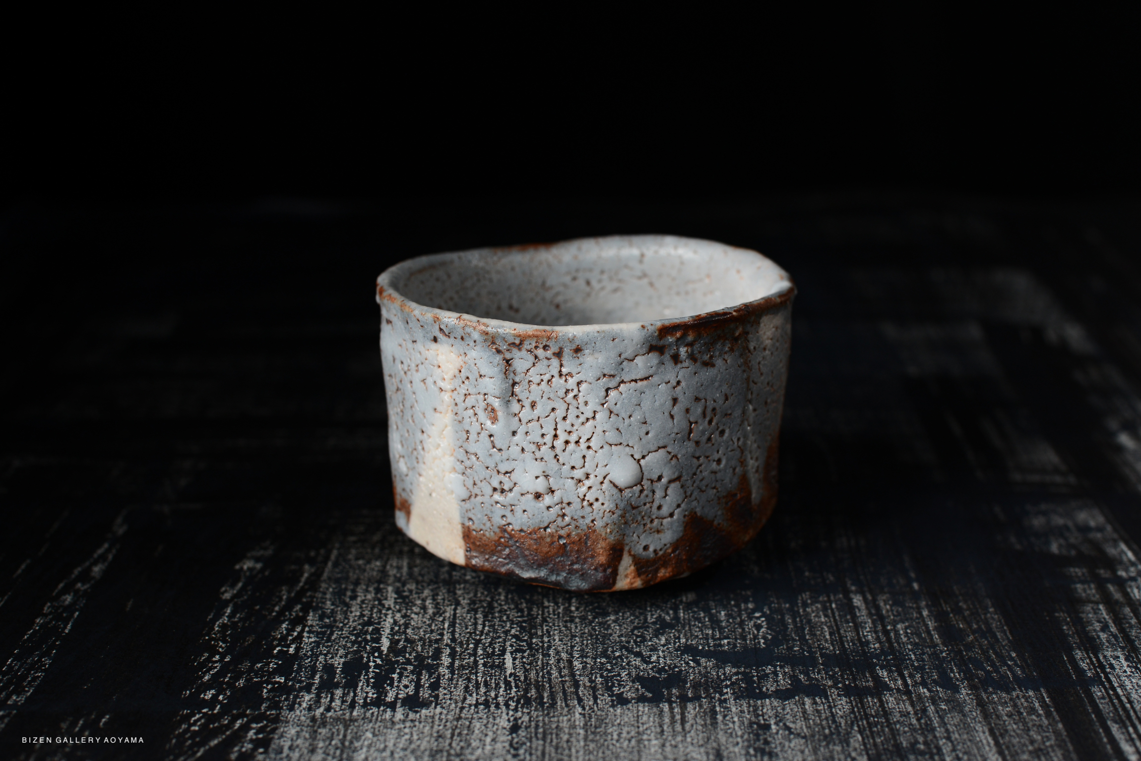 Shino Chawan tea bowl with a textured glaze and earthy colors, placed on a dark wooden surface.