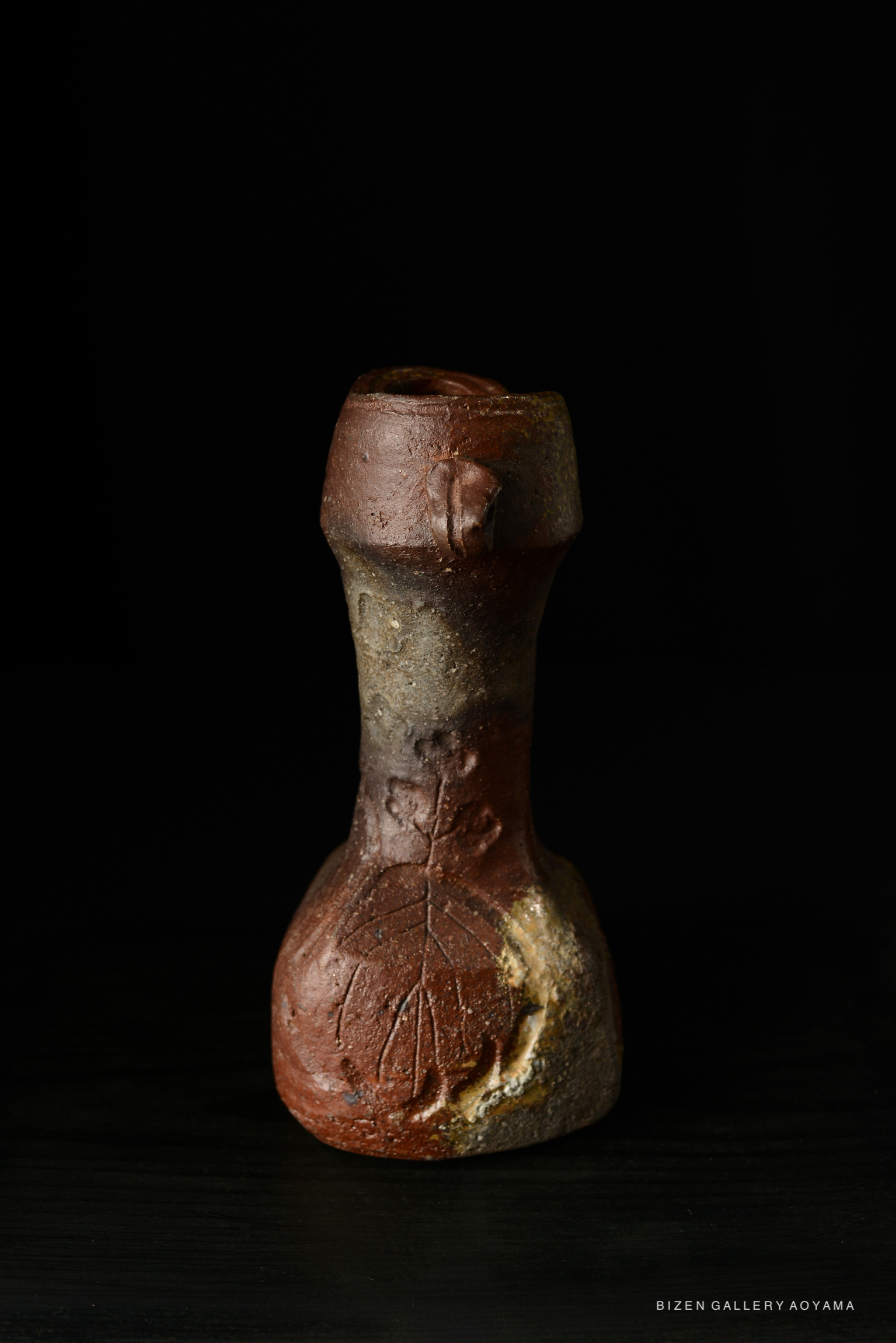 A Bizen pottery vase with a distinct leaf pattern, showcasing earthy tones and an elegant shape, displayed against a black background.