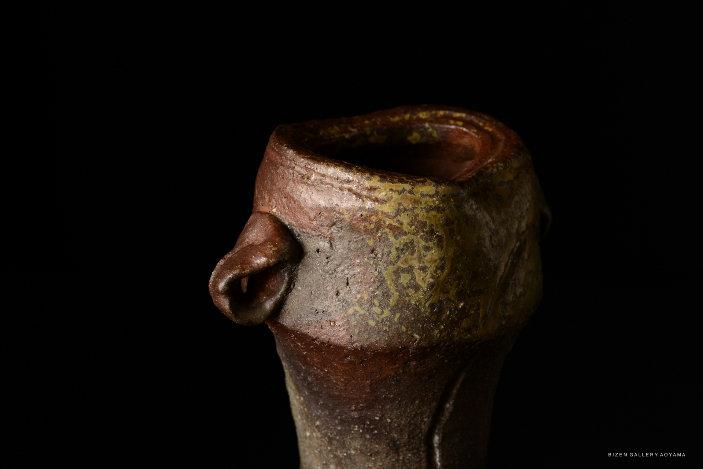 A close-up of a Bizen pottery vase with a textured surface and earthy tones, set against a black background.
