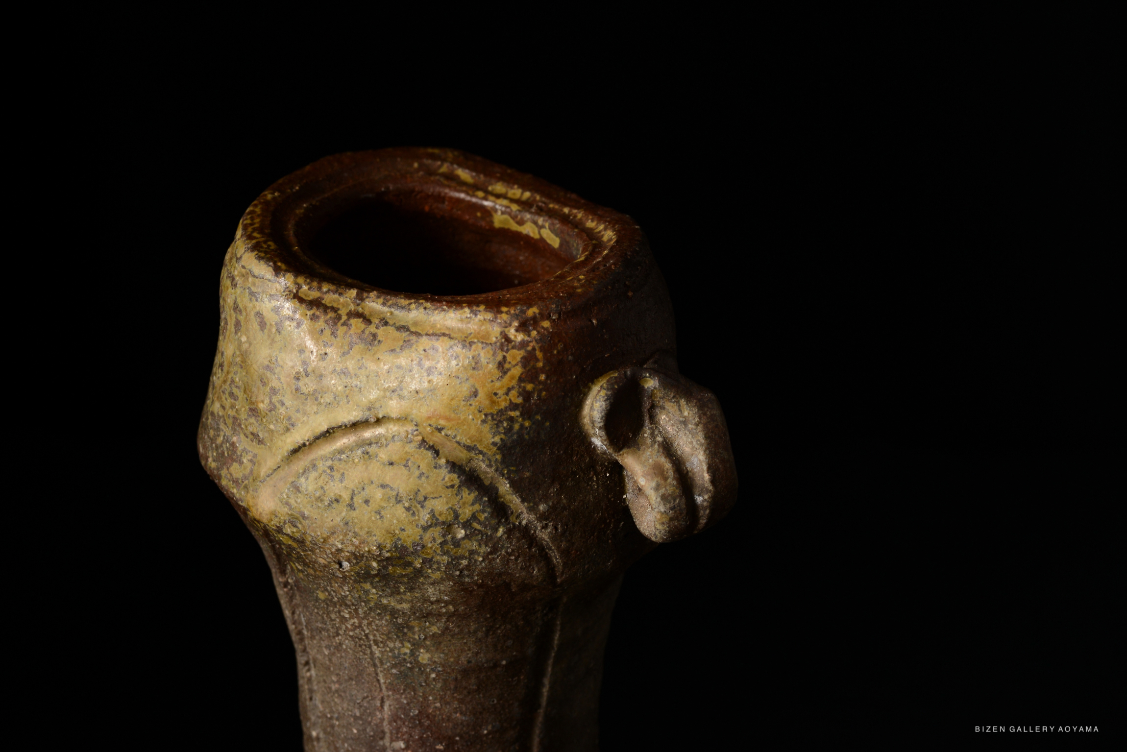 Close-up of a Bizen pottery vase with a unique lip and textured surface, set against a black background.