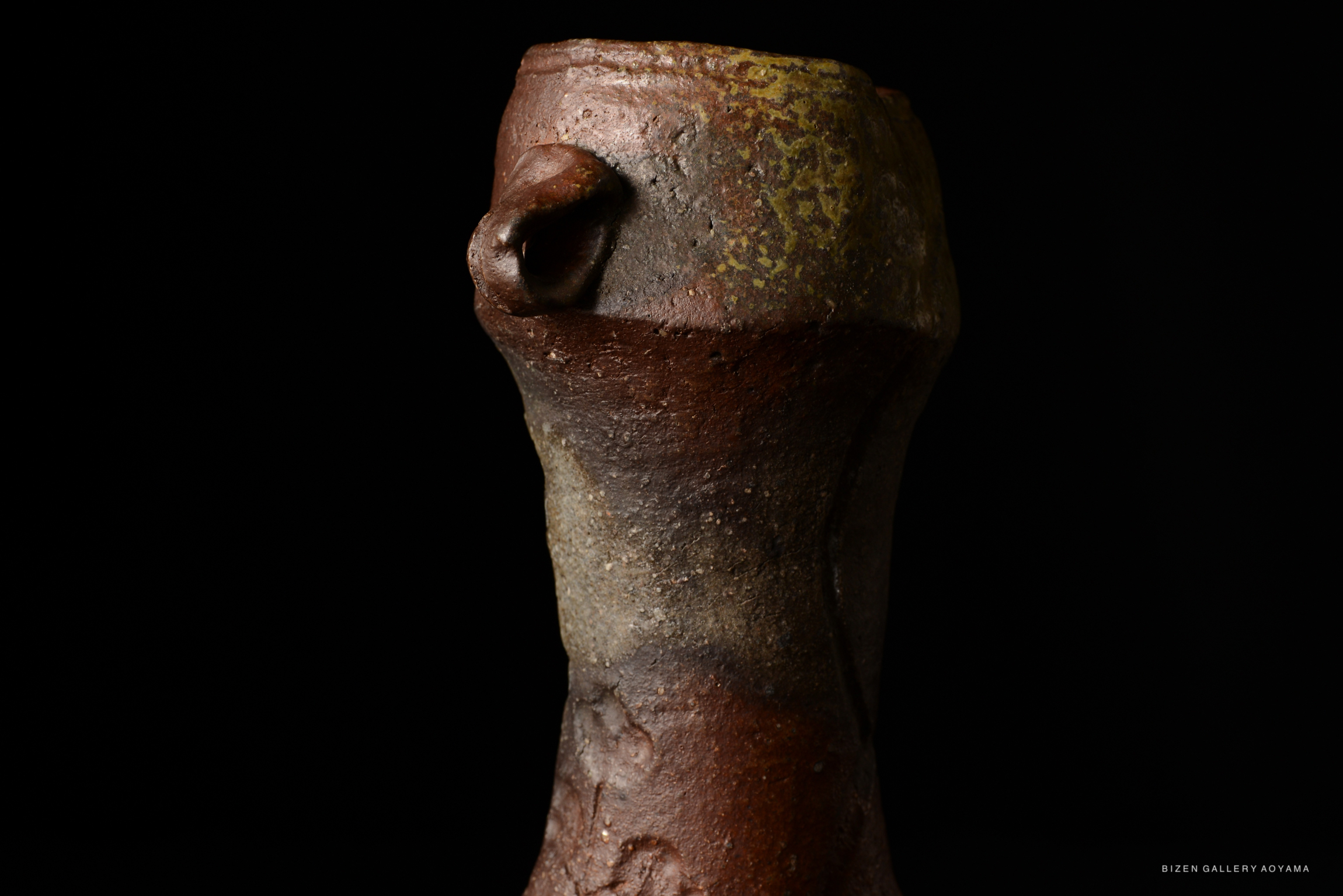 Close-up of a unique Bizen pottery vase with a textured surface and earthy tones, set against a black background.