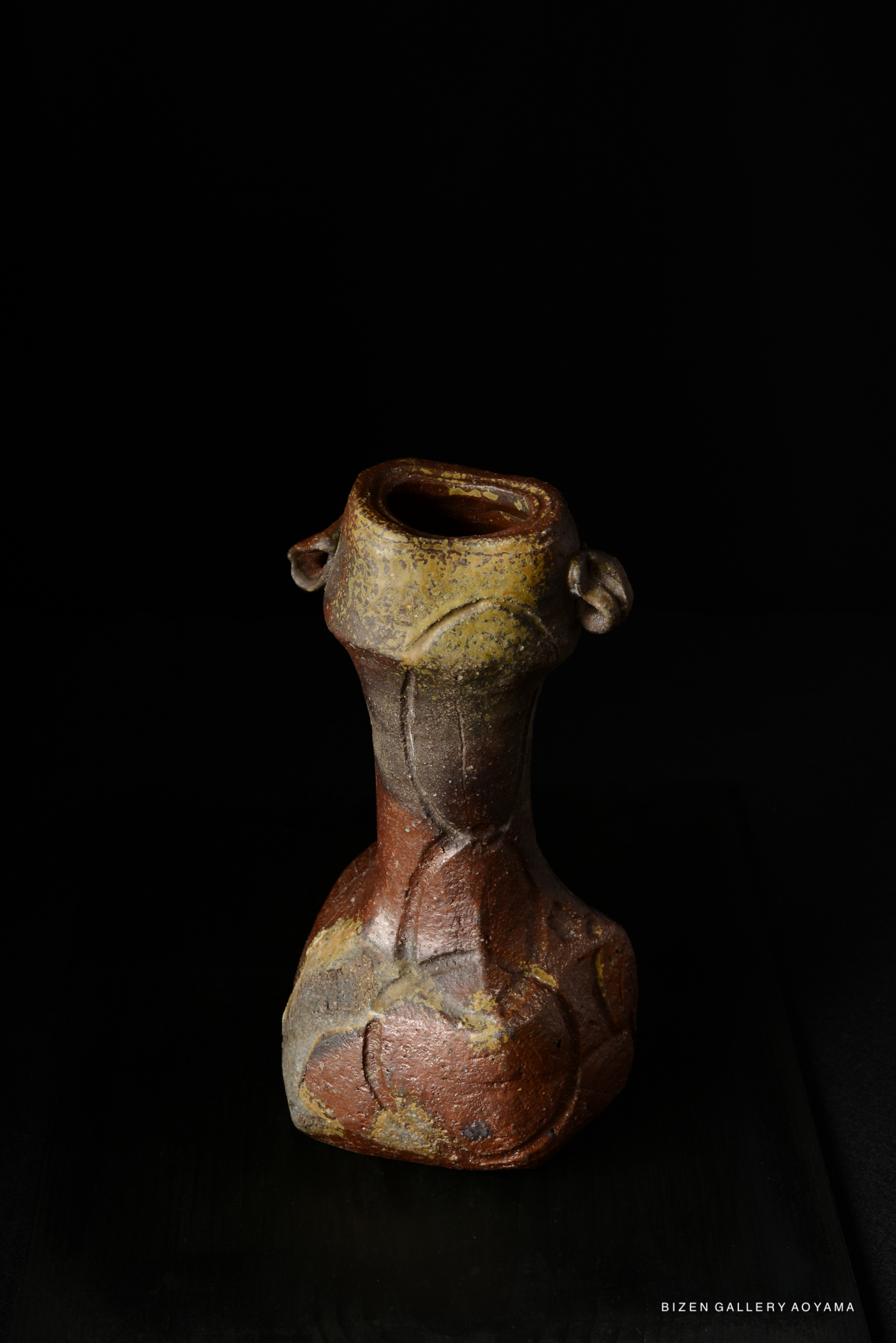 A Bizen pottery flower vase, featuring a distinctive shape with earthy tones, displayed against a dark background.