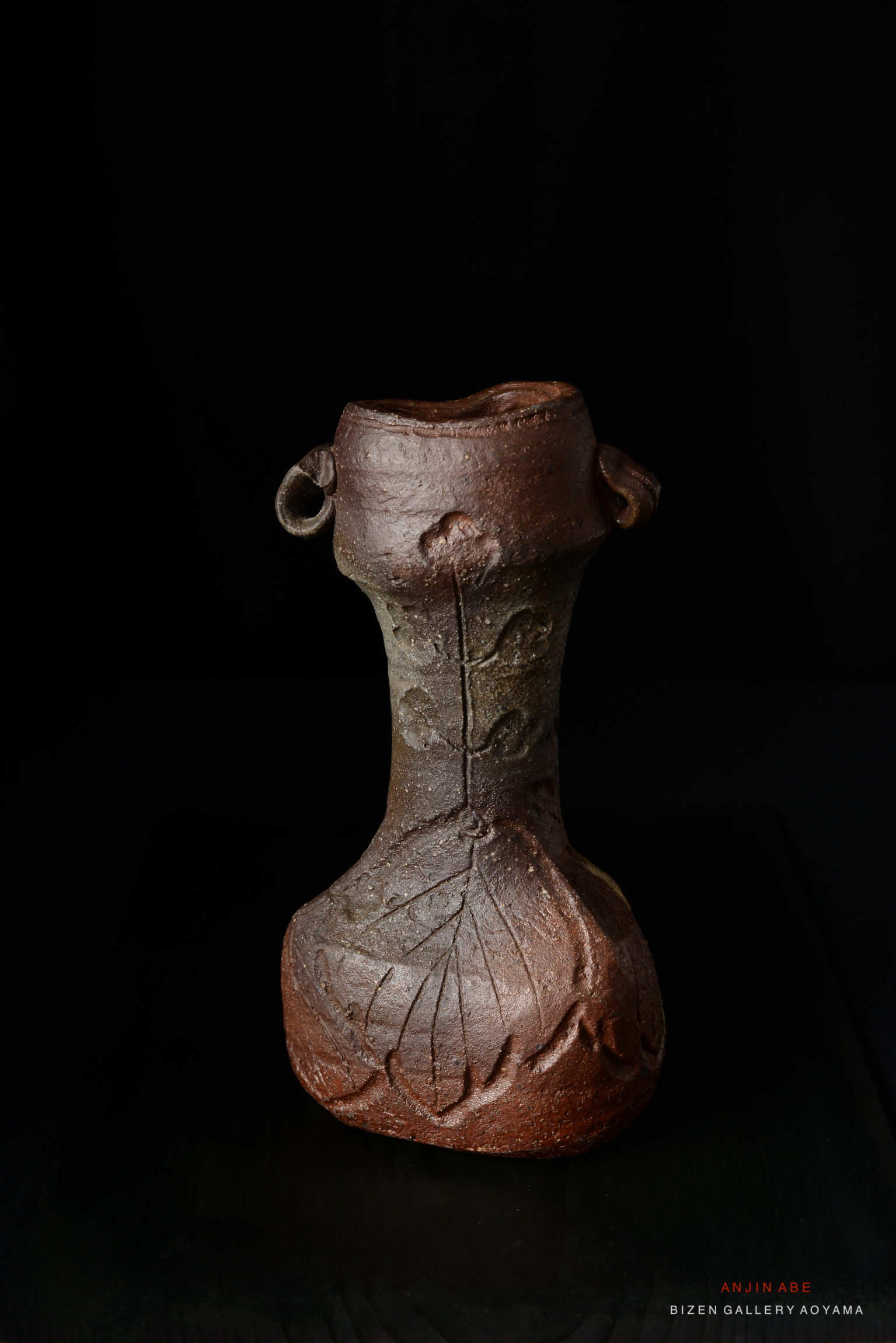 A textured ceramic vase with a leaf design, featuring two side handles, displayed against a black background.