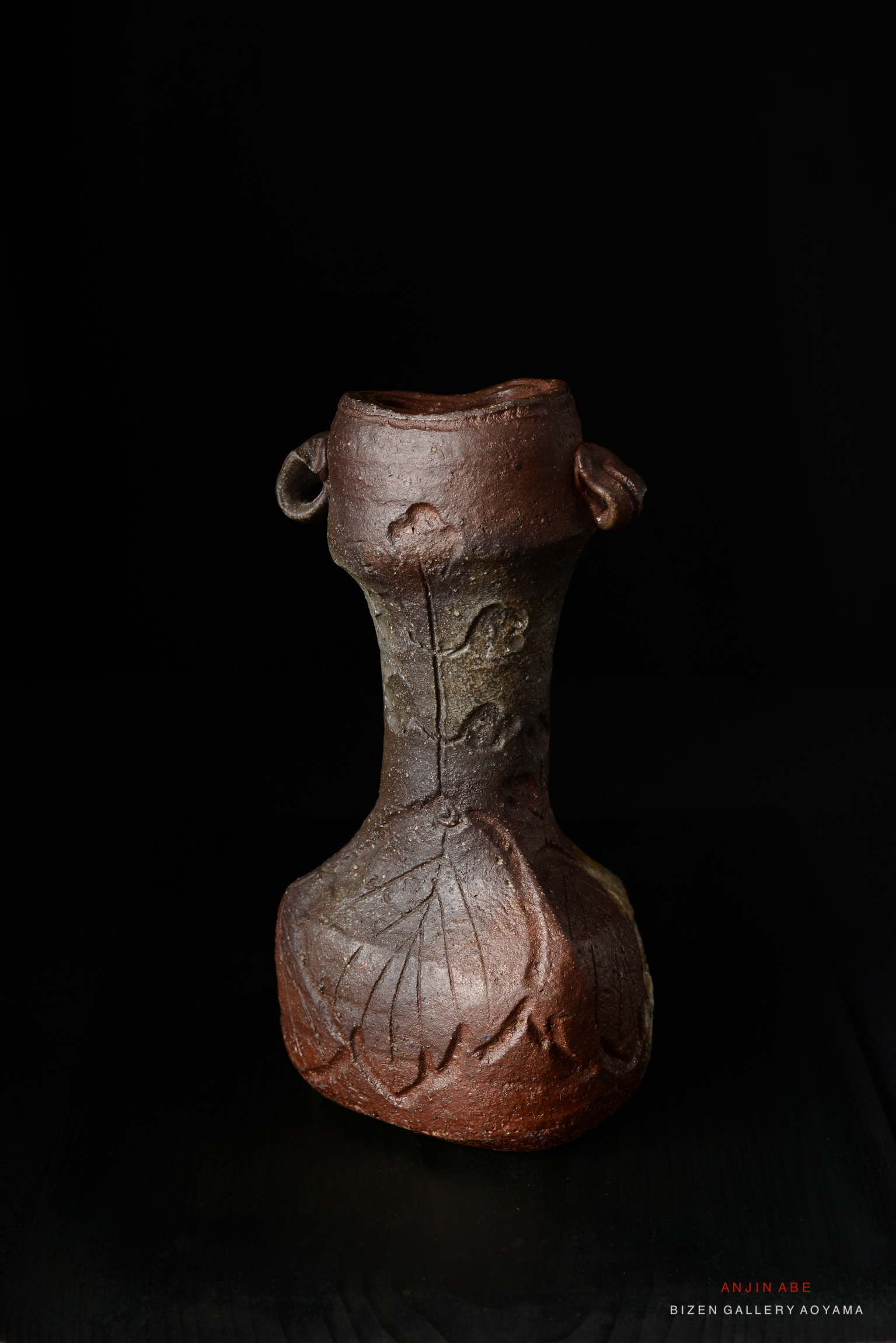 A handcrafted Bizen ware flower vase with a unique curved shape and textured leaf motifs, displayed on a dark background.