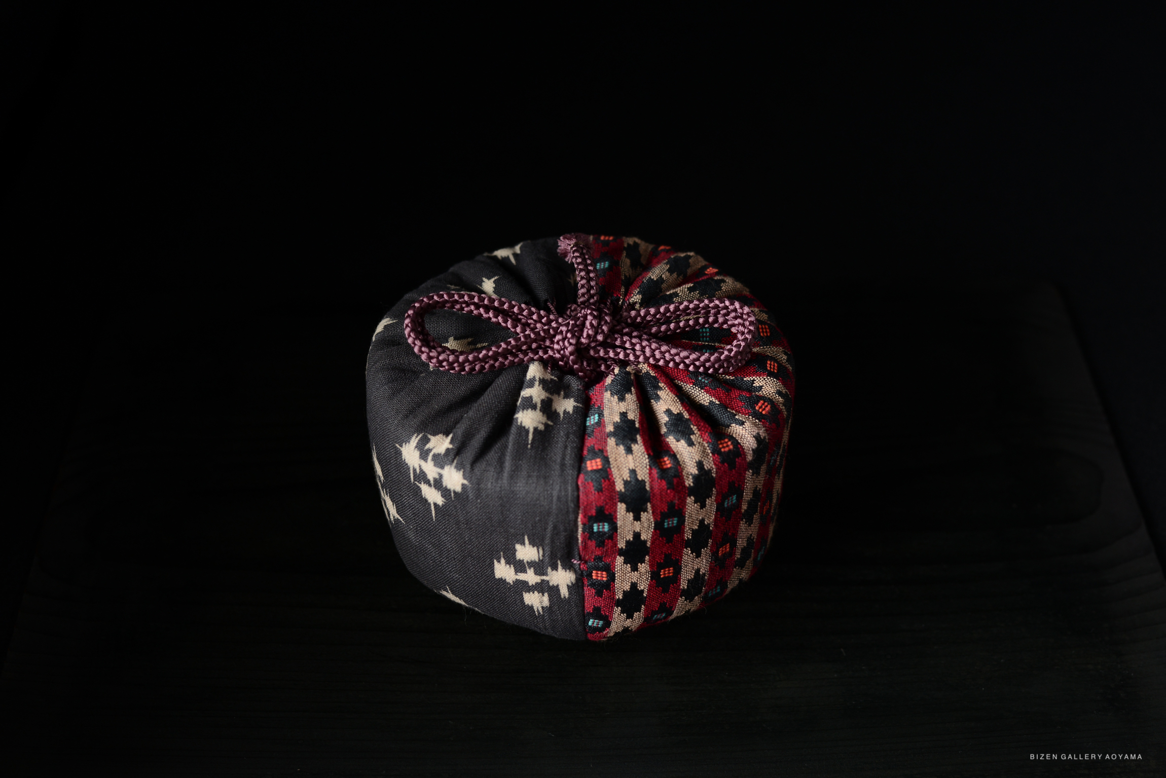 A beautifully patterned fabric pouch tied with a purple cord, displayed against a dark background.