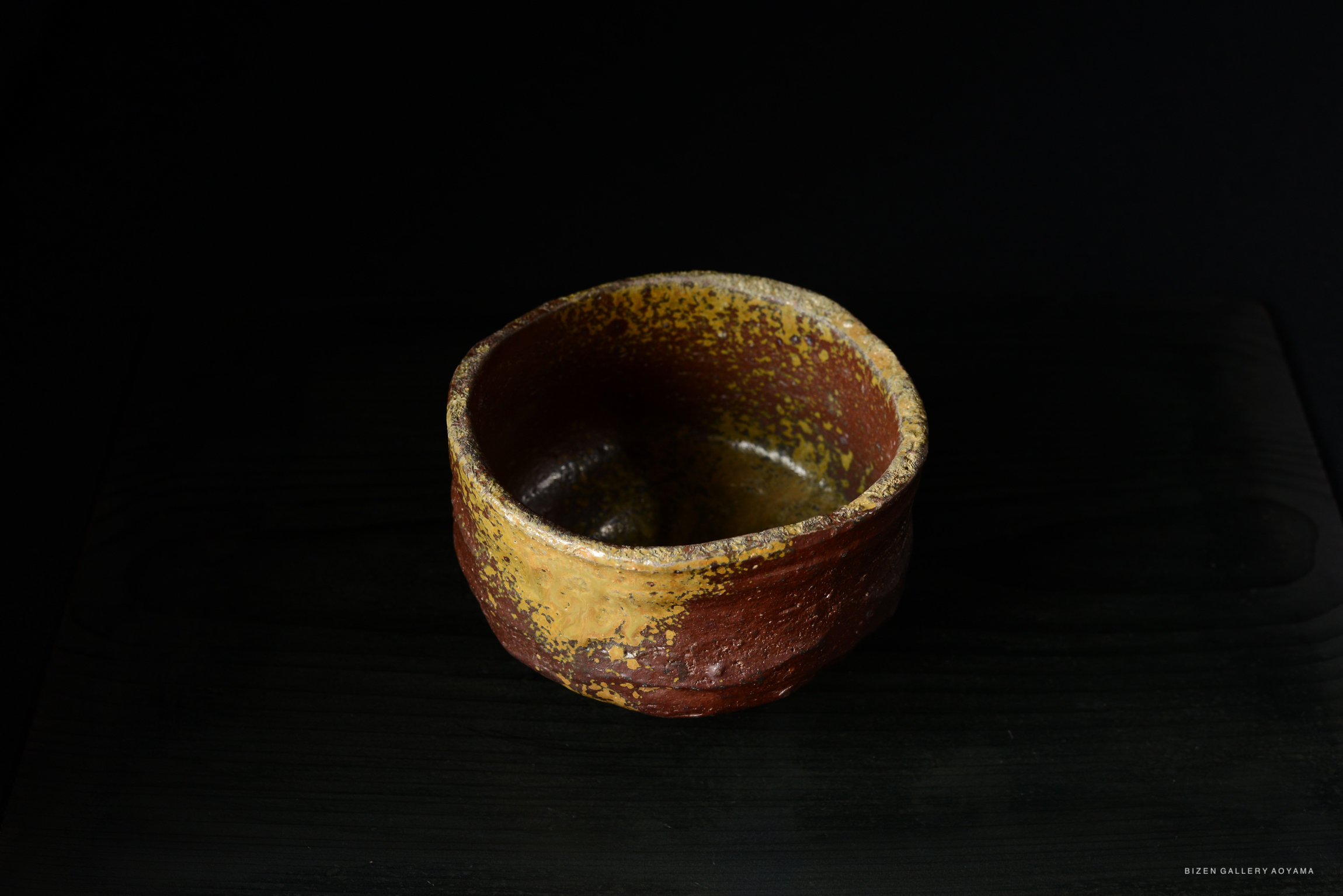 A rustic, handmade ceramic bowl with a textured surface and earthy colors, set against a dark background.
