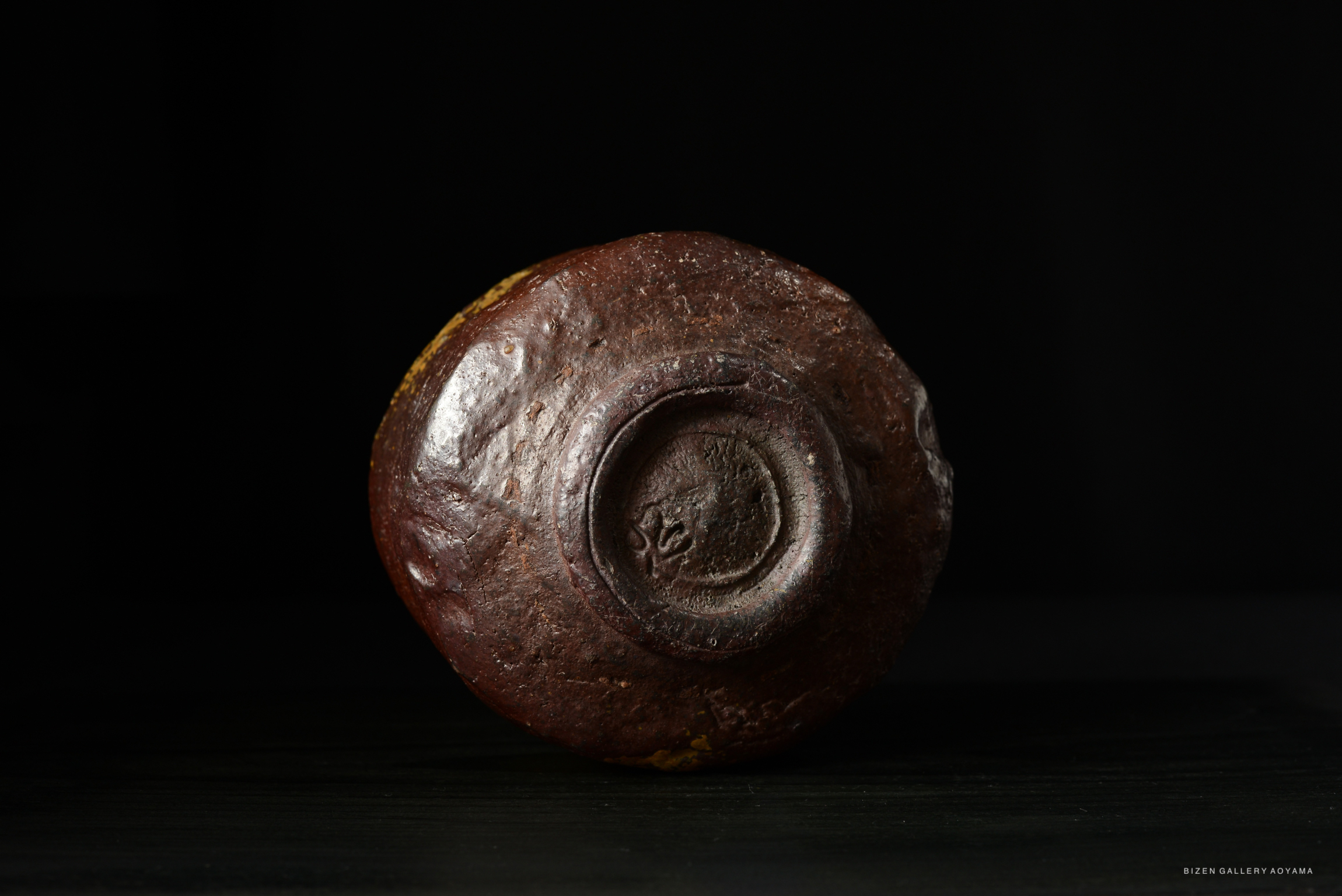 A close-up view of the bottom of a round, textured pottery piece, showing a circular indentation and a dark brown surface against a black background.