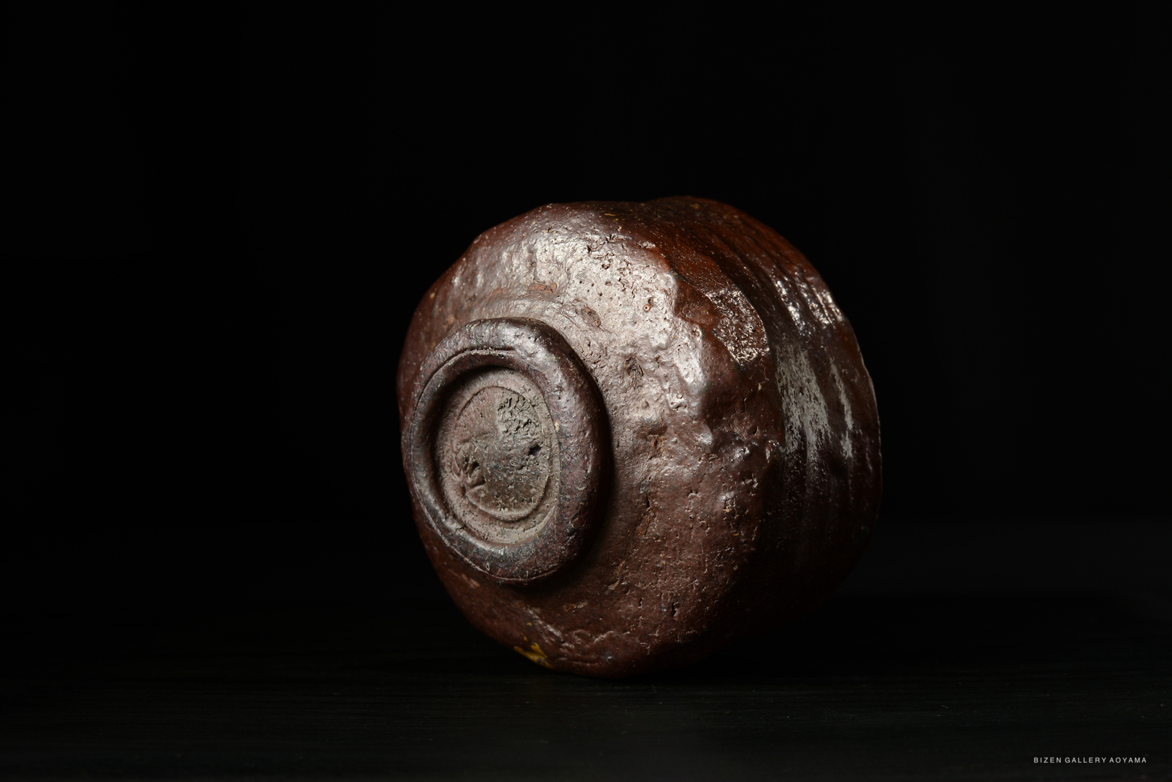A close-up view of a round, textured pottery piece set against a dark background.