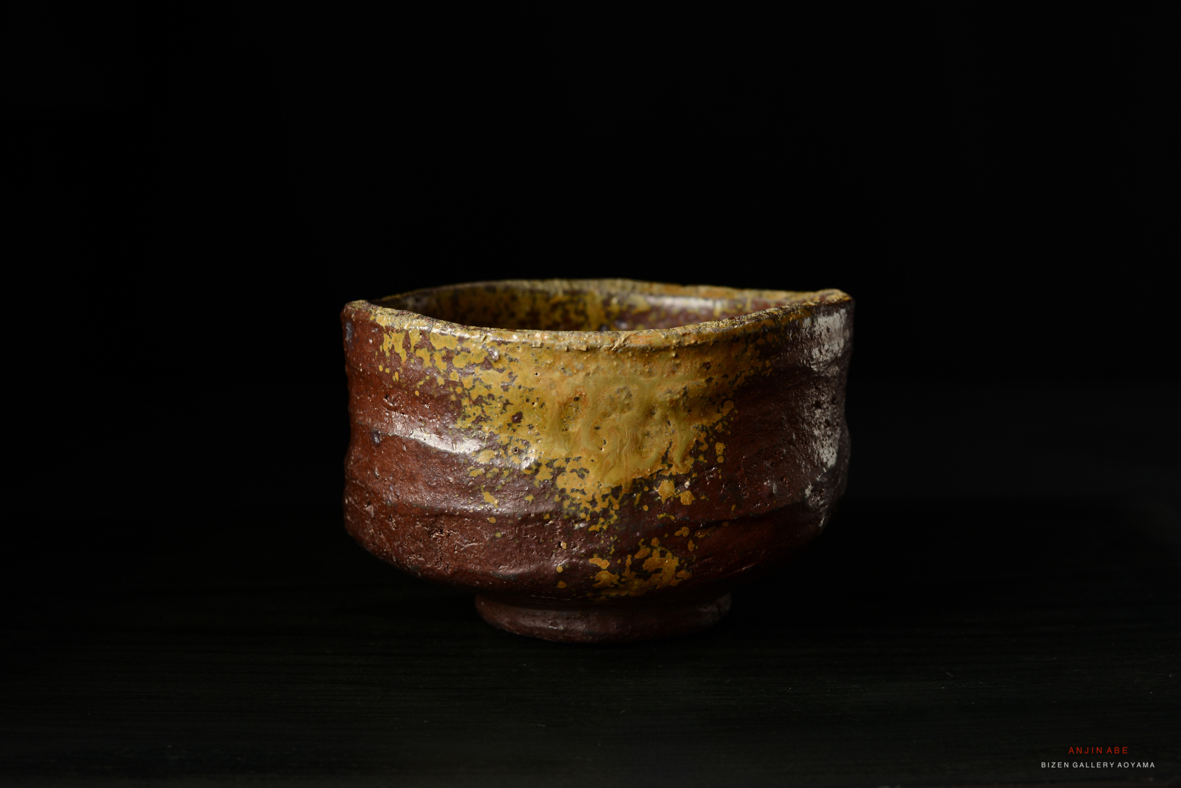 A close-up view of a ceramic bowl with a textured surface, featuring a blend of brown and yellow hues, set against a black background.