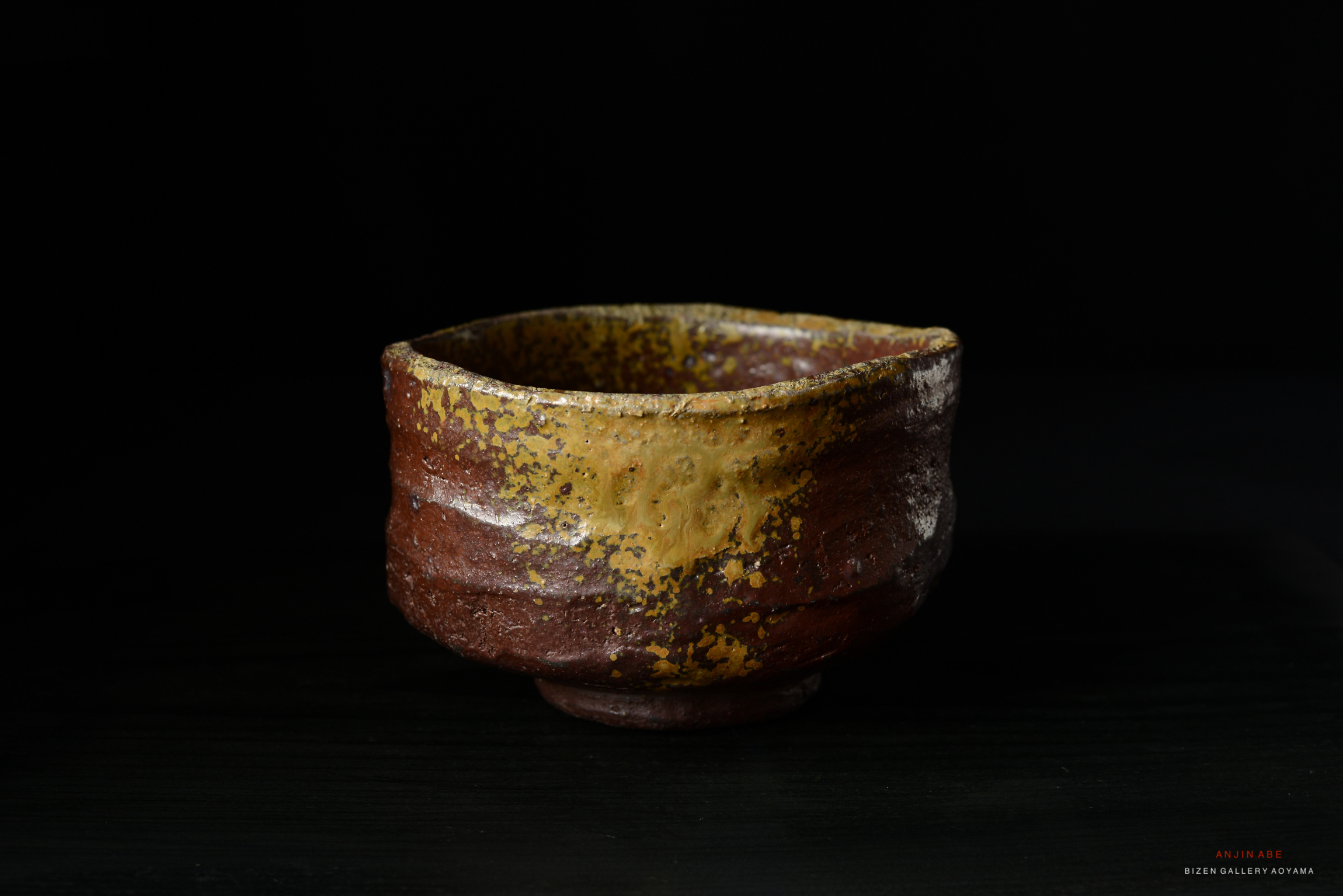 A rustic ceramic bowl with a textured surface featuring earthy tones of brown and yellow, set against a dark background.
