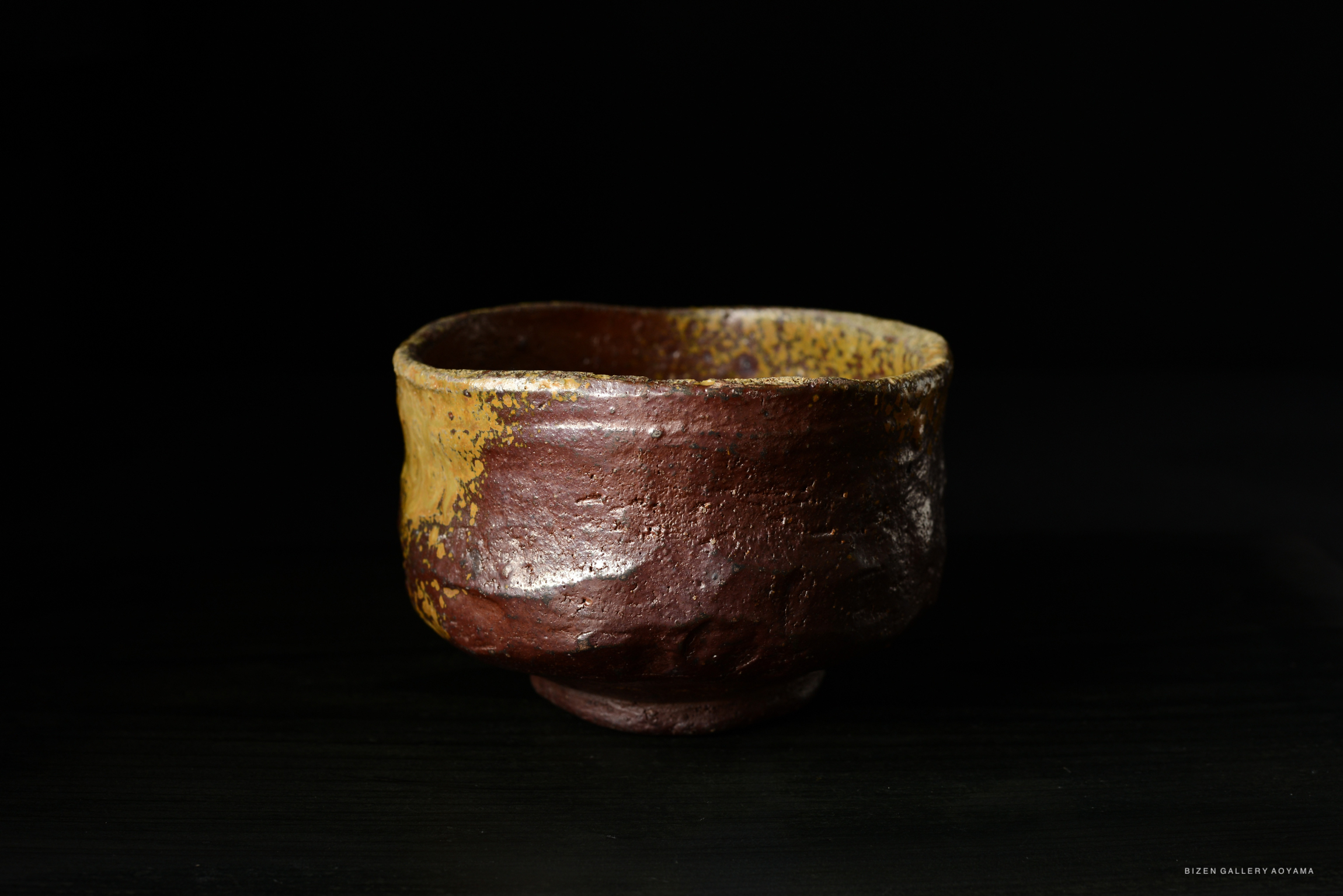 A rustic, handcrafted ceramic bowl with a textured exterior in shades of brown and yellow, set against a black background.