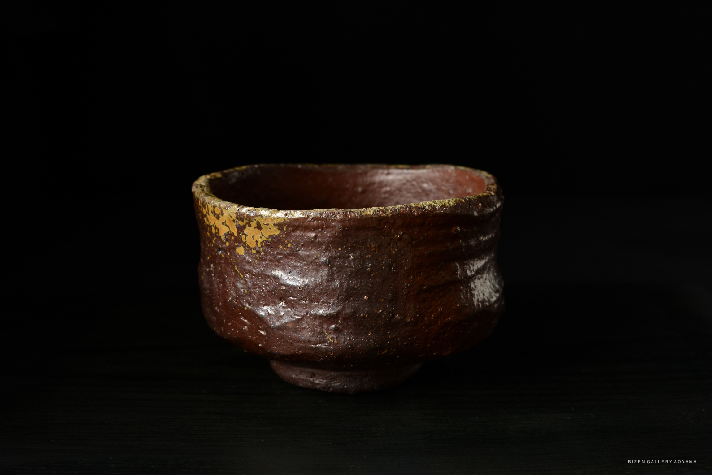 A rustic brown pottery bowl with a textured surface and a chipped golden rim, set against a dark background.