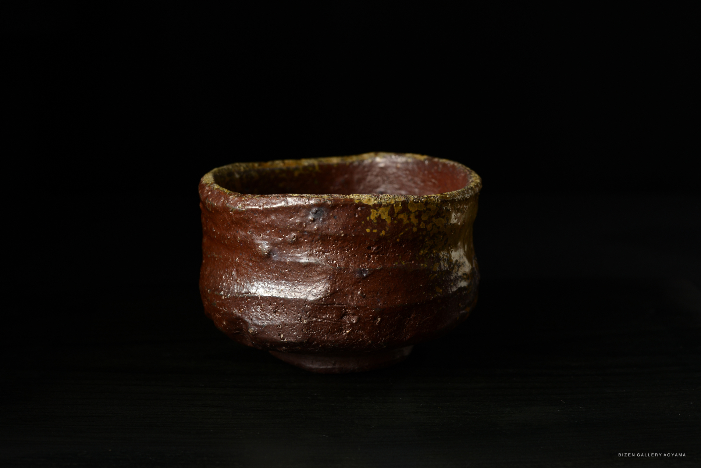 A textured brown ceramic bowl with a slightly irregular shape and a yellow rim, set against a dark background.