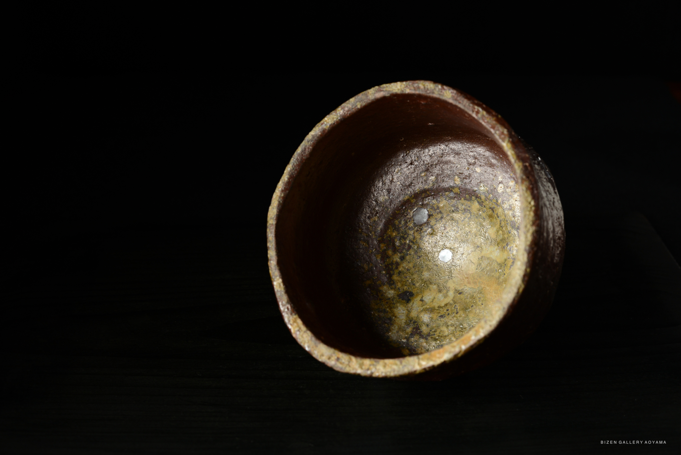 A close-up view of an intricately textured ceramic bowl set against a dark background, showing its inner surface with a noticeable shine.