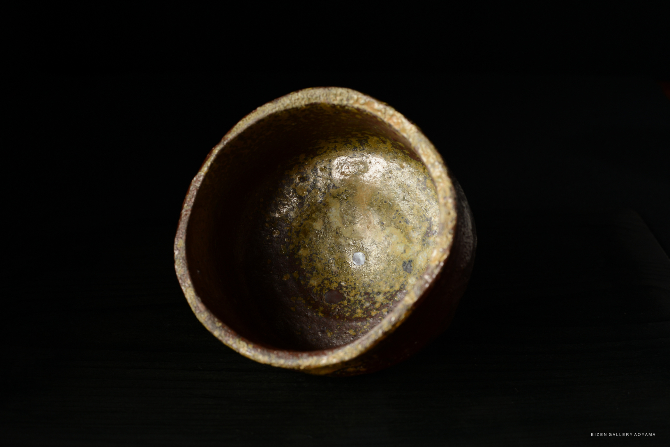 A close-up view of an ancient ceramic bowl with a textured, rustic surface, showing a rich brown color and a shiny, metallic inner finish.