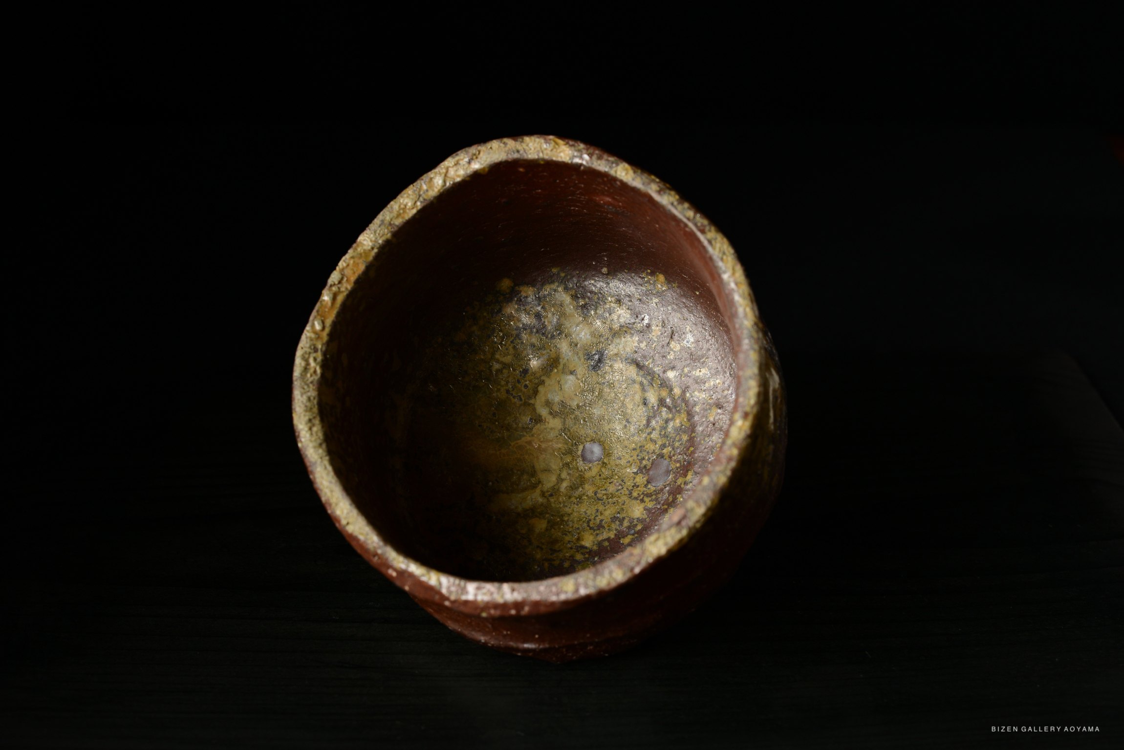 A close-up view of a rustic, traditional ceramic bowl with a textured surface and earthy tones, set against a dark background.