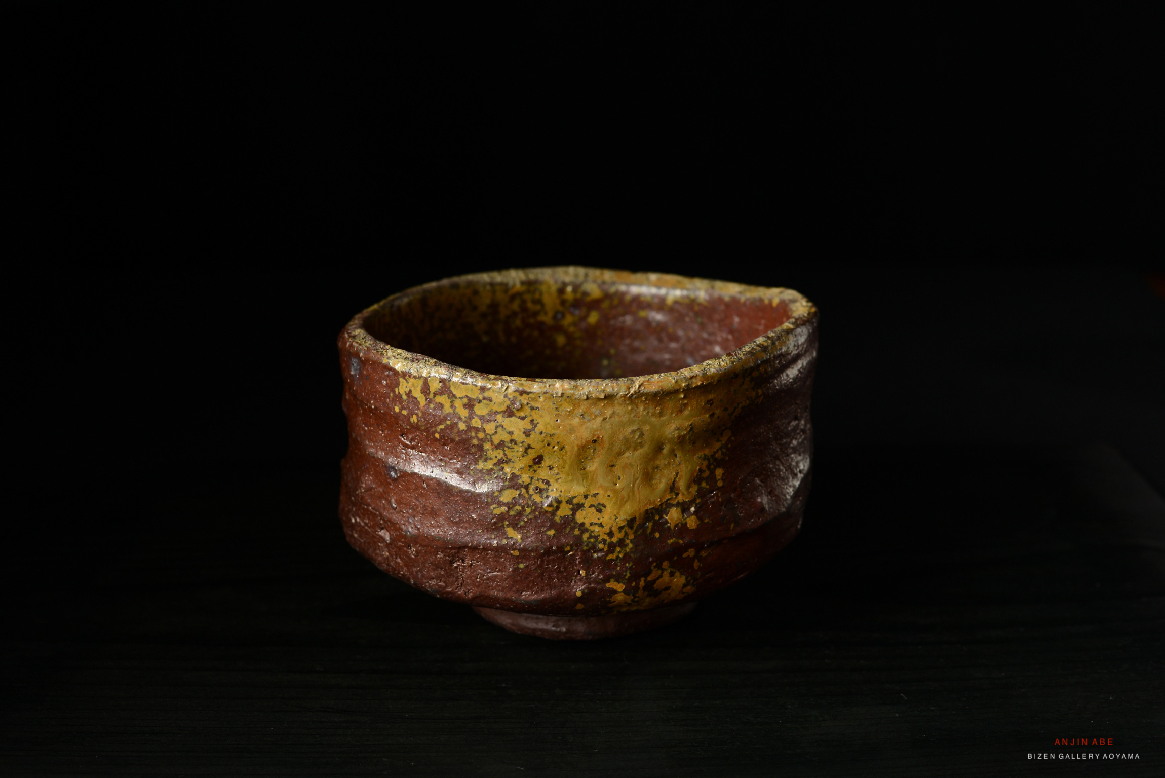 A handcrafted ceramic bowl with a textured, earthy surface featuring red and yellow hues.