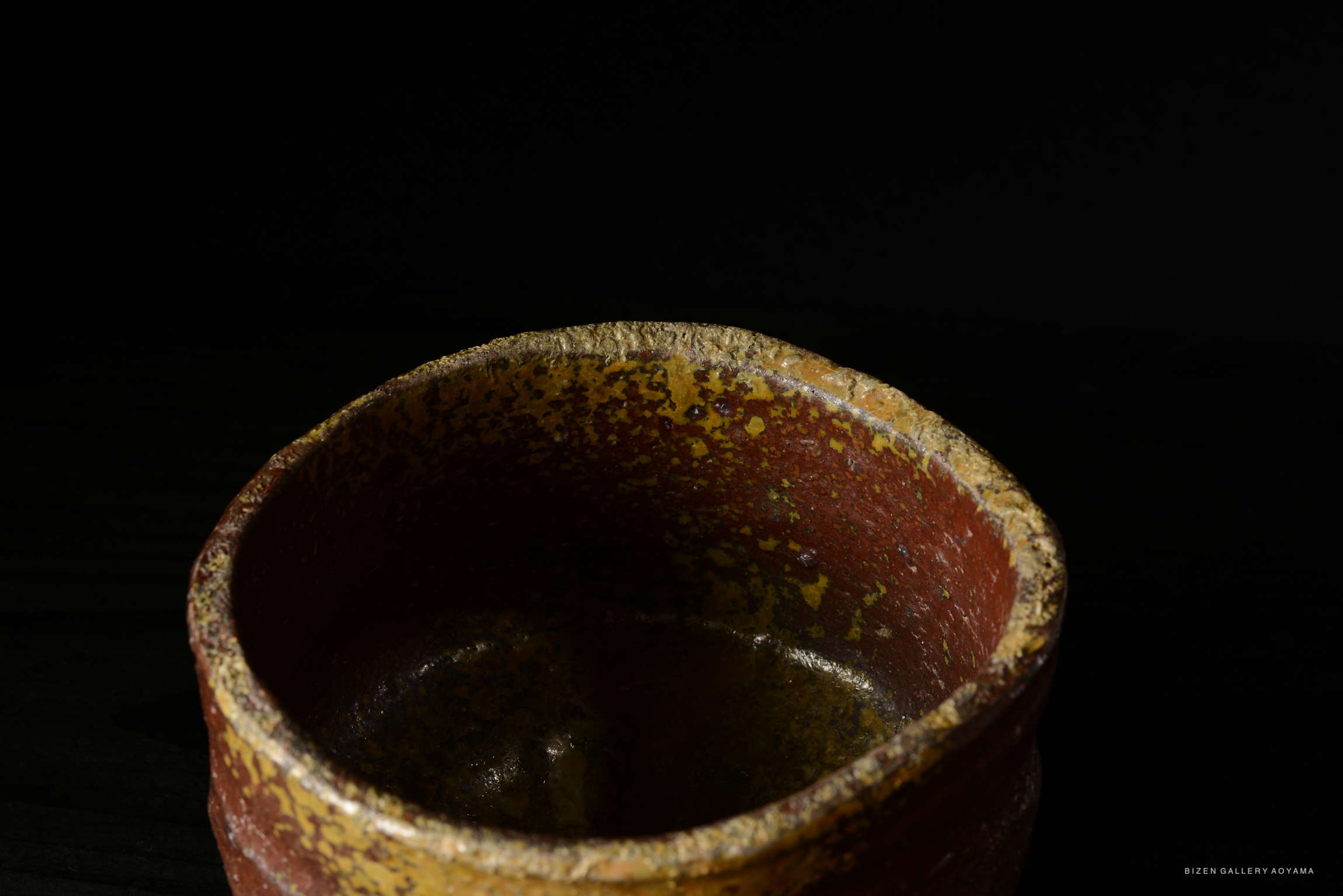 Close-up of a rustic ceramic pot with a textured surface, set against a dark background.