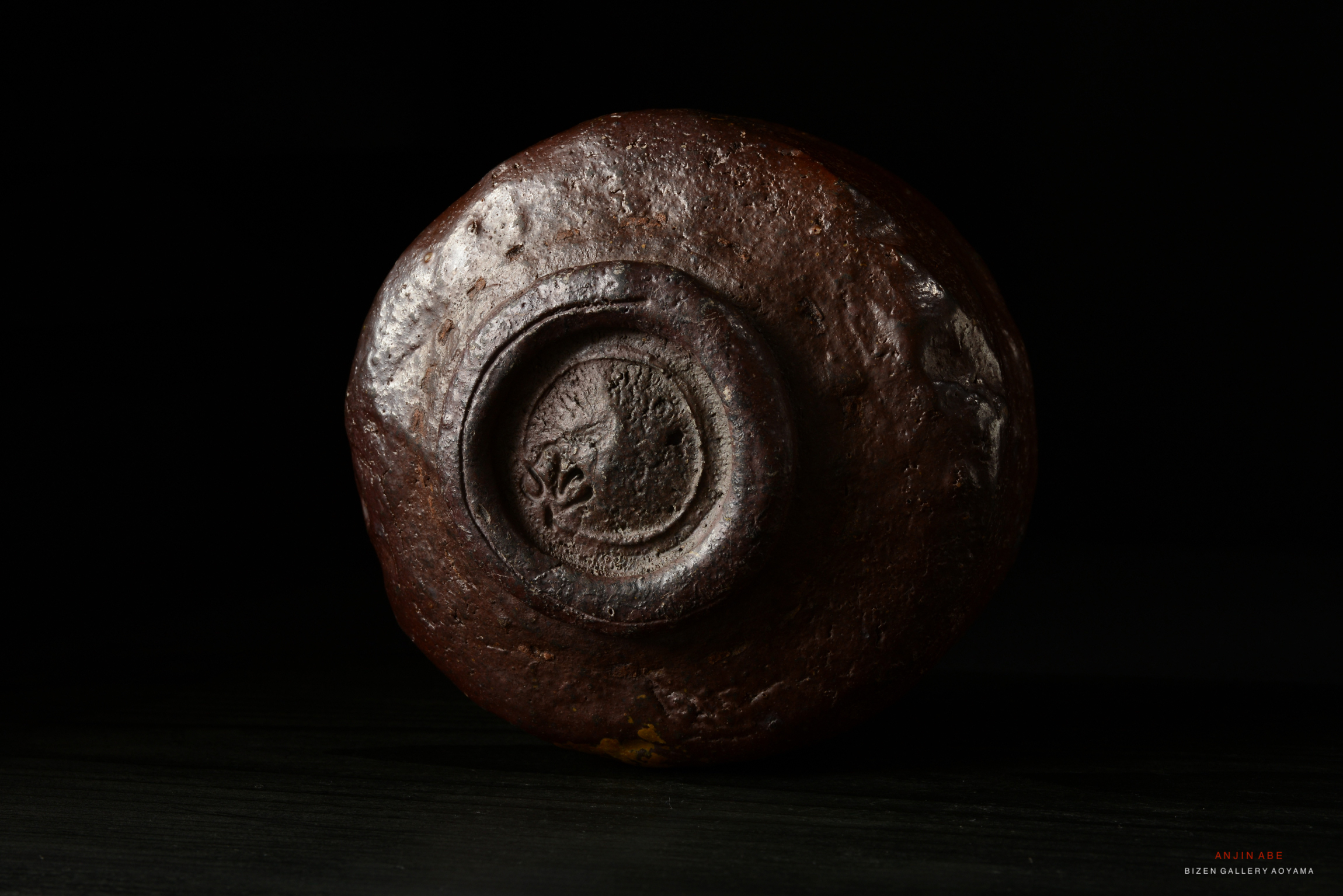 Close-up view of a circular brown ceramic piece with an embossed design in the center, set against a dark background.