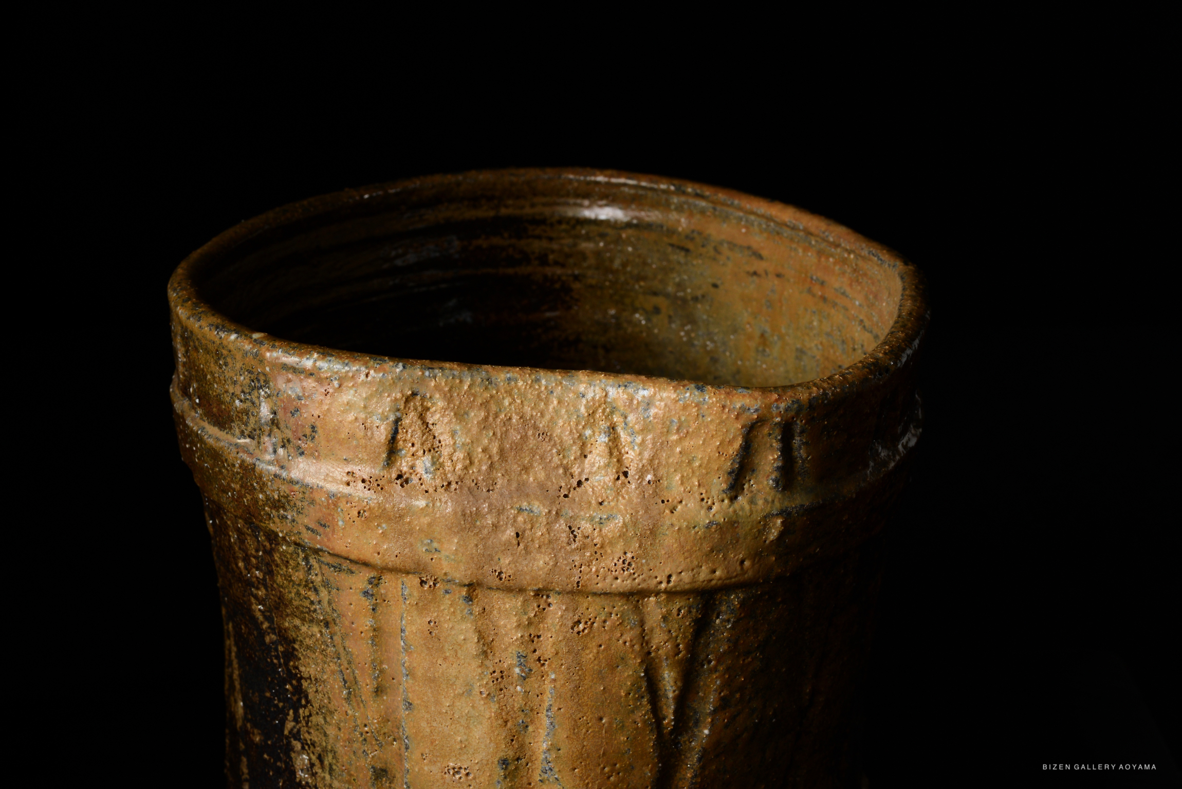 Close-up of a traditional Bizen pottery Mizusashi, showcasing its earthy textures and rich brown tones against a black background.
