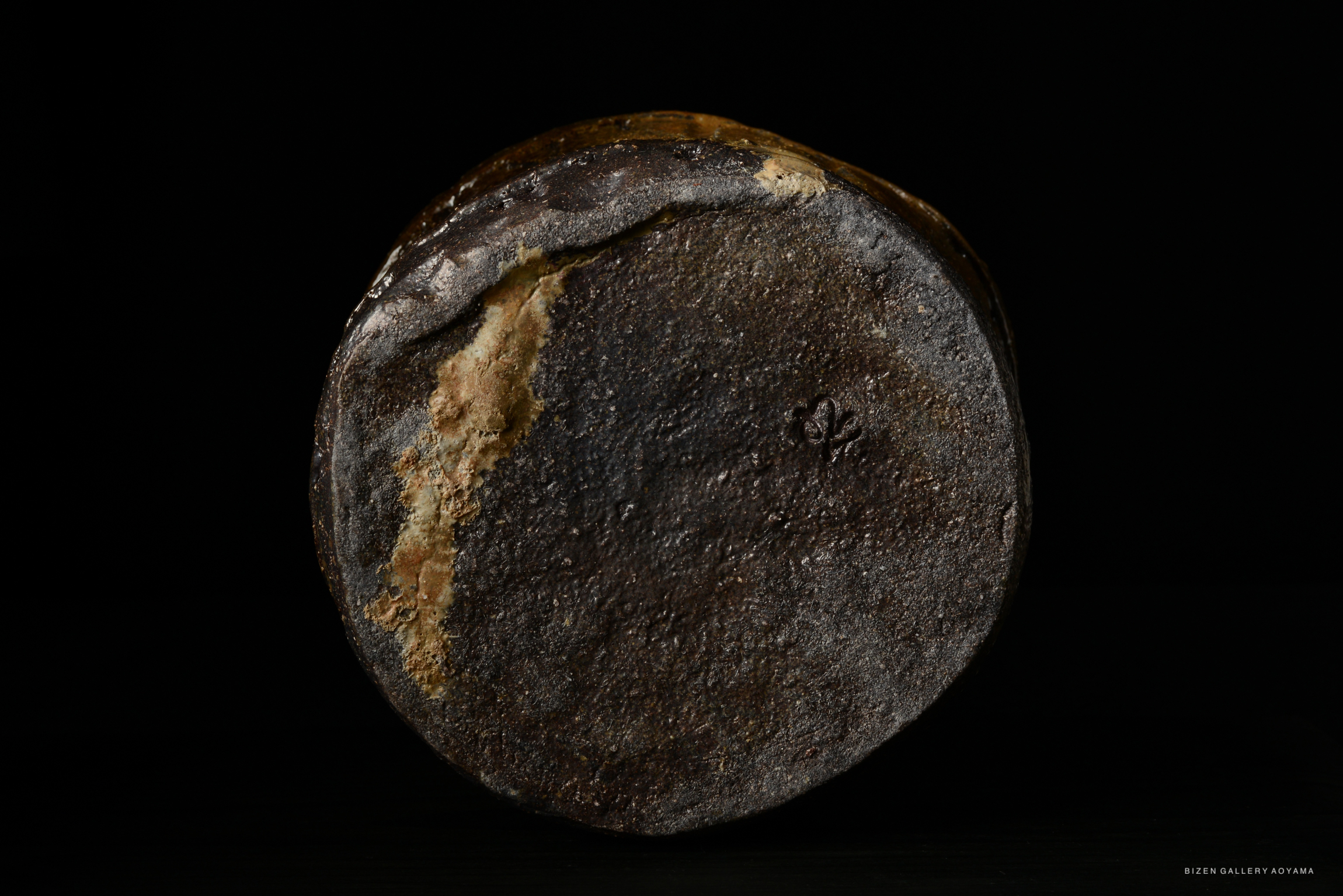 A close-up view of the bottom of a ceramic piece, showcasing a textured, dark surface with a small emblem or mark visible.