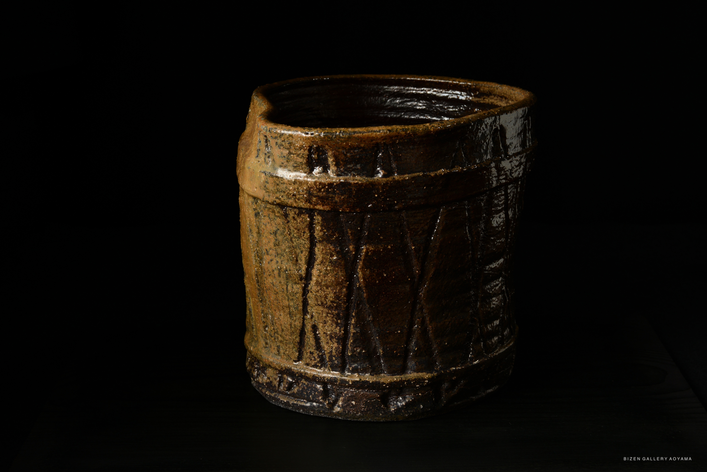 A traditional Japanese Mizusashi, a water container, crafted from clay with a textured surface and a dark glaze, designed in a barrel shape.