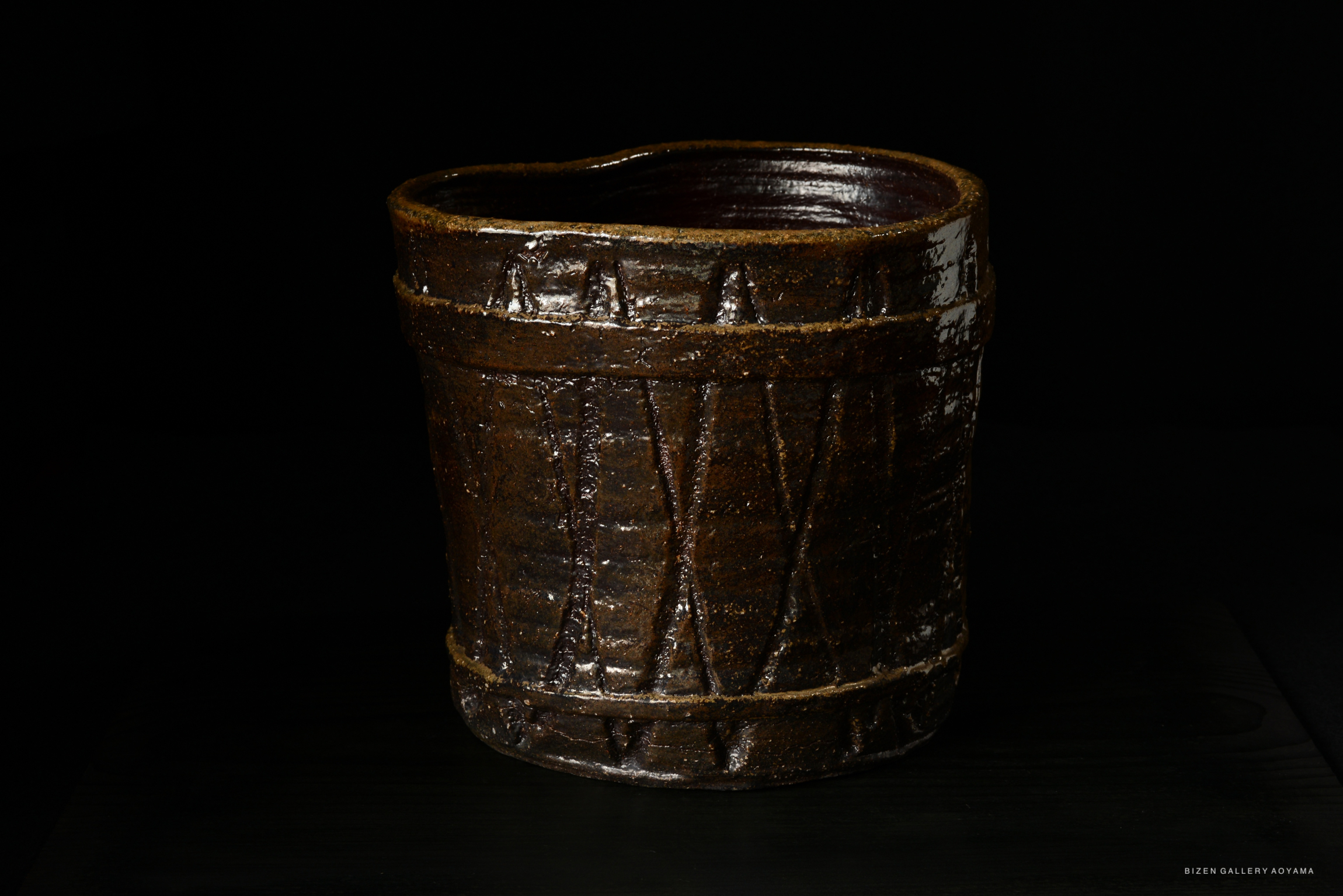 A handcrafted Bizen pottery mizusashi with a dark brown glaze, featuring textured patterns and a slightly irregular shape.