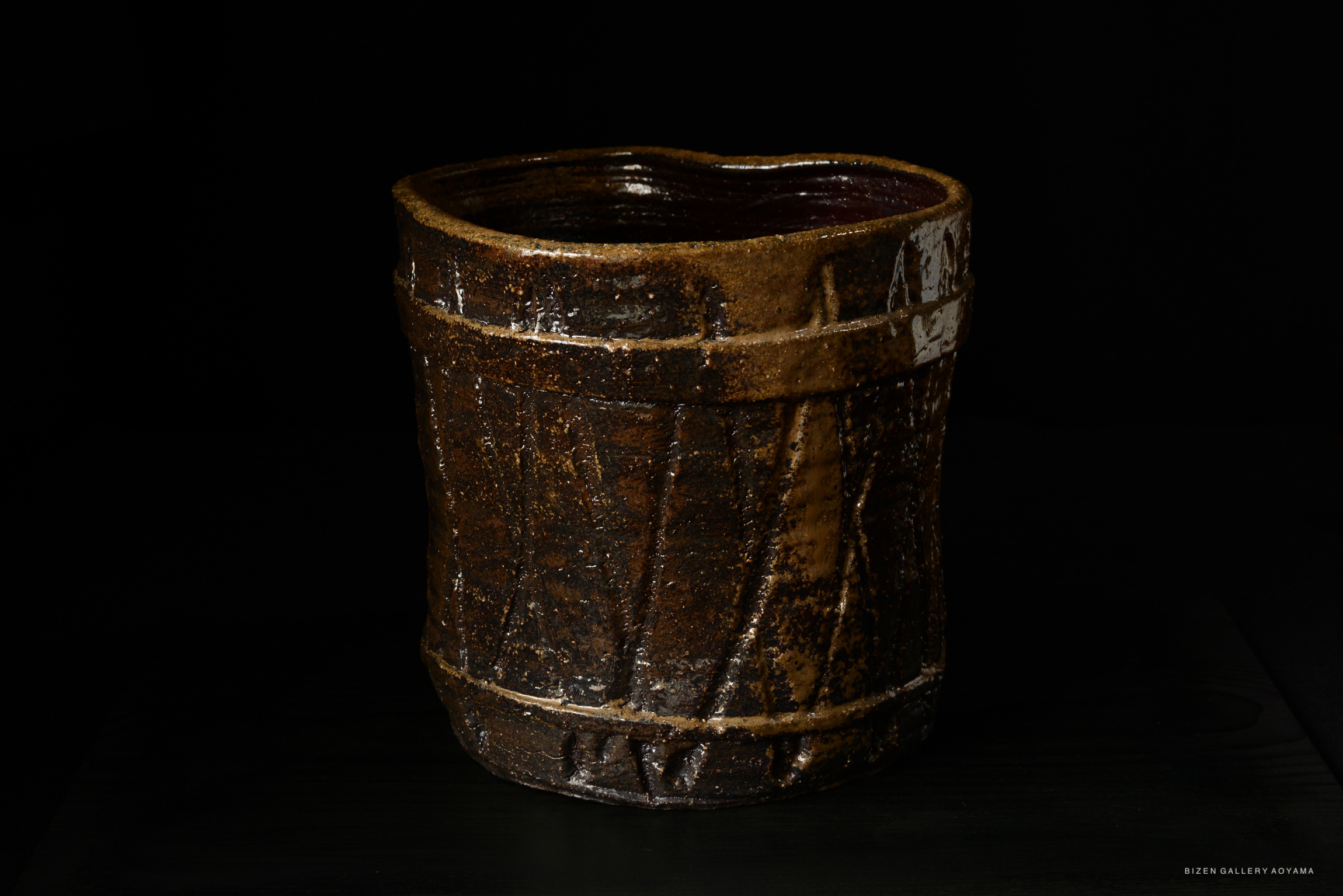 A rustic, handcrafted ceramic mizusashi (water container) in dark brown with a textured surface, showcasing a traditional design.