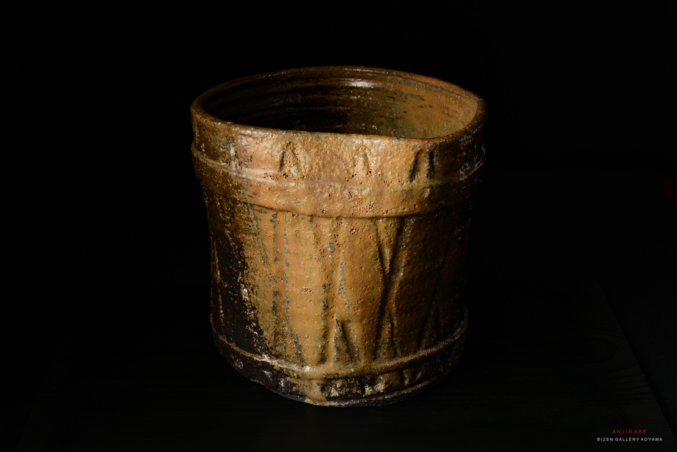 A traditional Bizen pottery mizusashi, featuring a textured surface with earthy tones, displayed against a dark background.