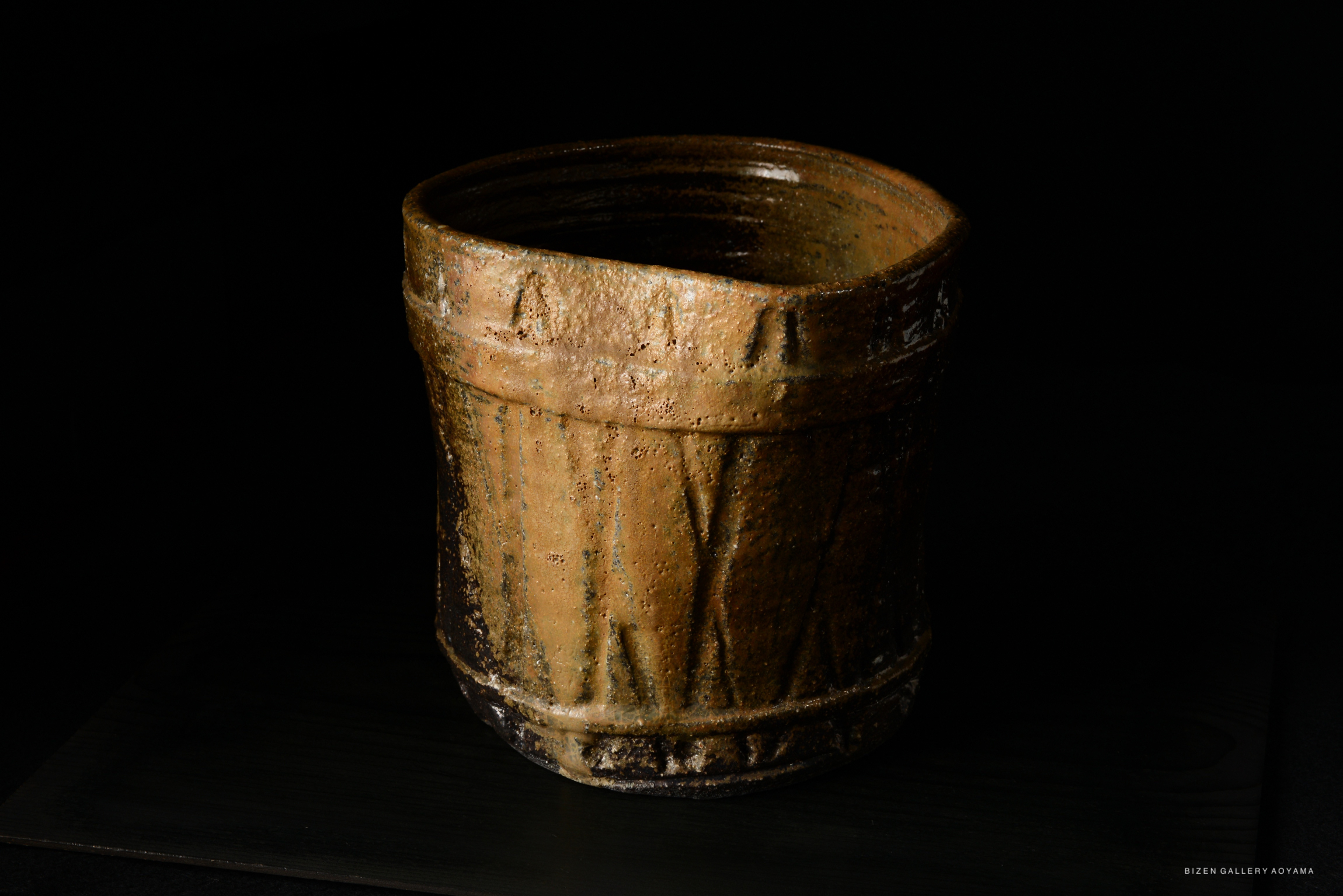 A close-up image of a uniquely shaped ceramic vessel with a textured surface, featuring earthy tones and intricate designs, set against a dark background.