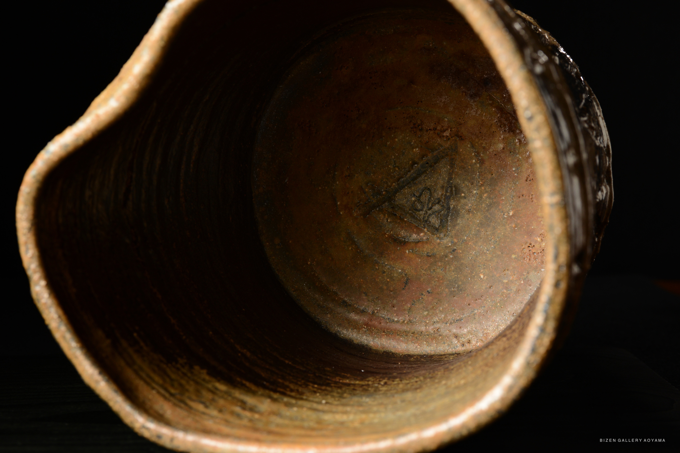 Inside view of a ceramic mizusashi (water container) showcasing its earthy textures and a subtle triangular mark at the bottom.