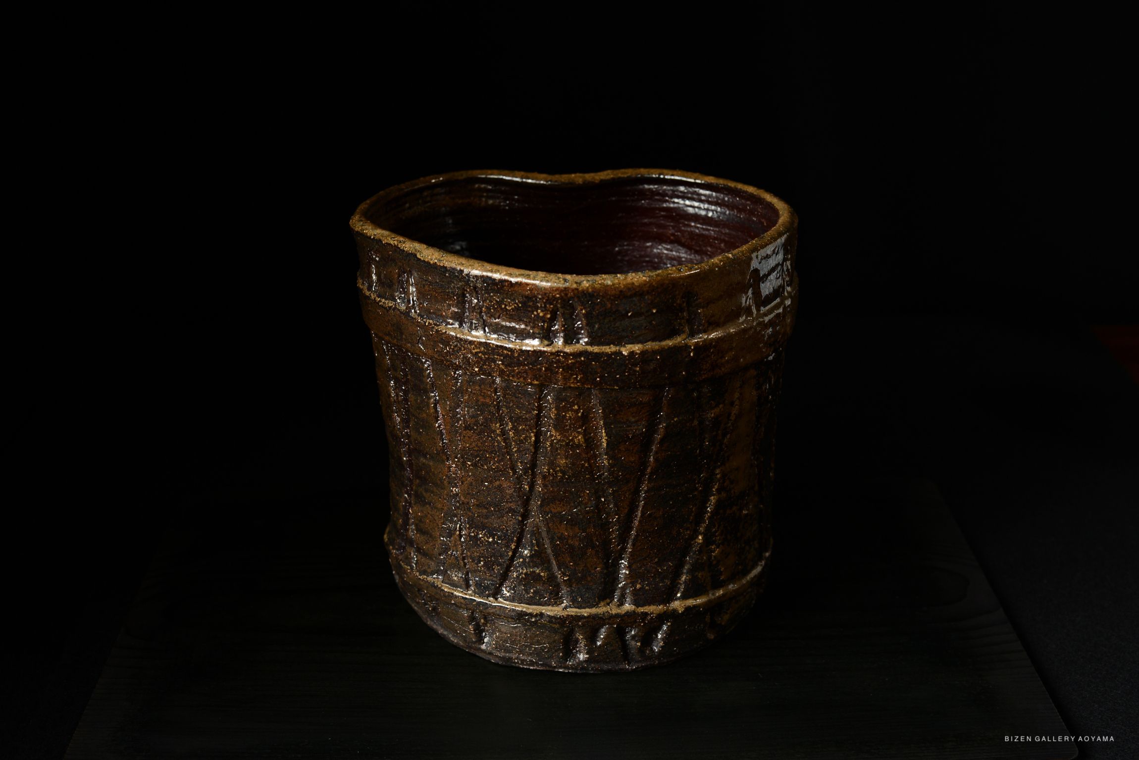 A handcrafted Bizen pottery mizusashi (water container) with a rustic brown finish and traditional textured patterns, displayed against a dark background.