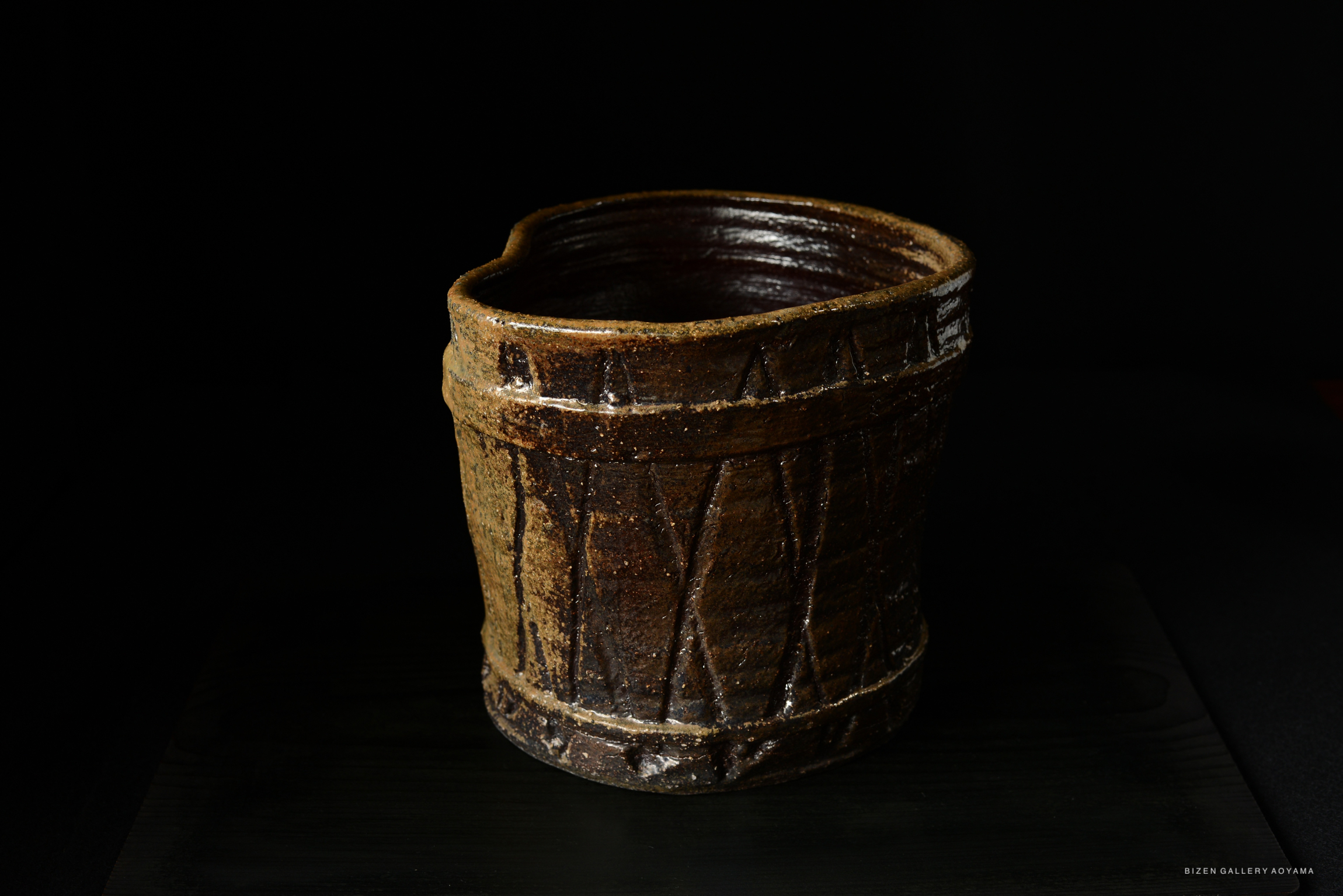 A handcrafted Bizen pottery mizusashi, a traditional Japanese water container, showcasing a textured surface and earthy tones, positioned against a dark background.