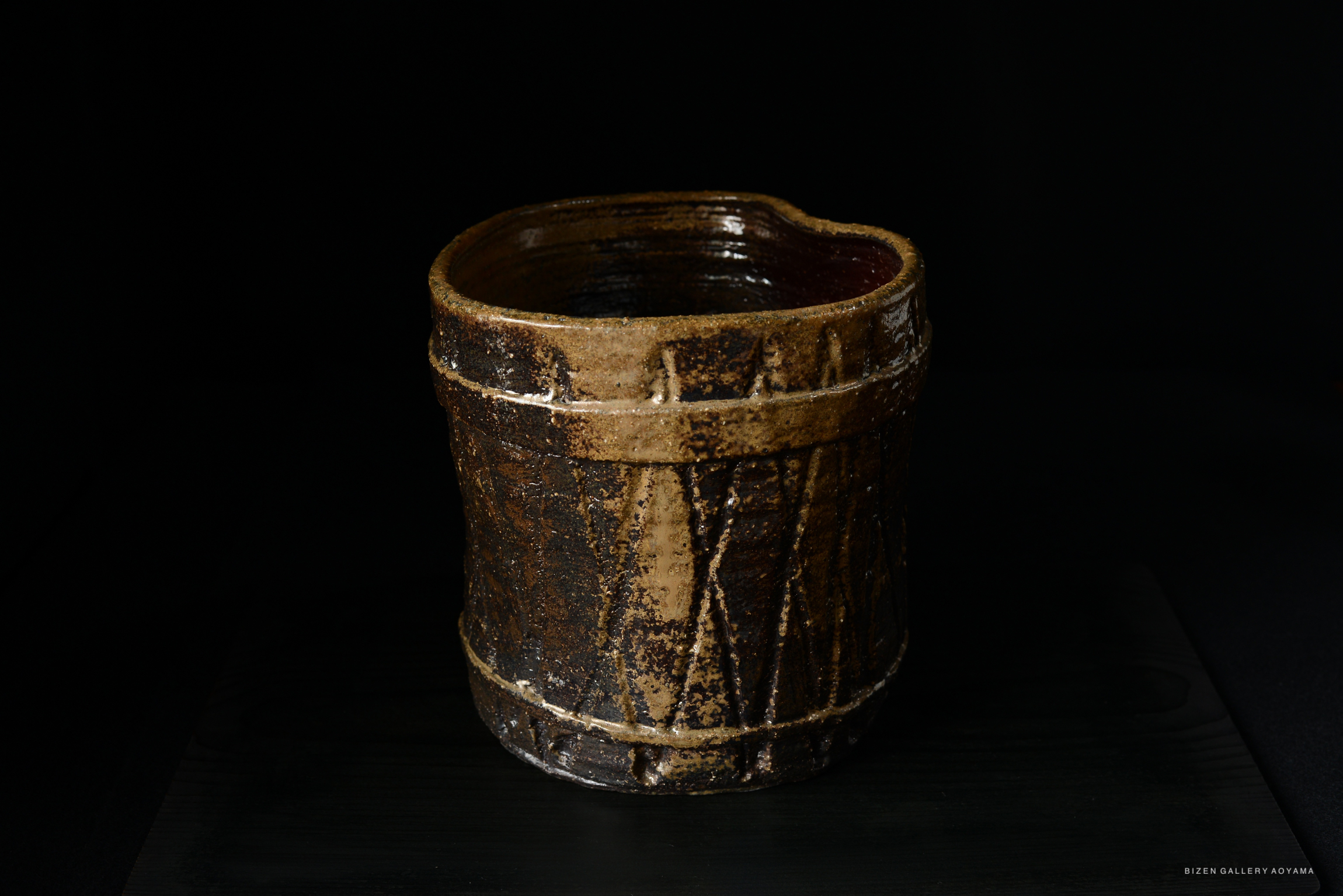 A close-up view of a traditional ceramic Mizusashi, featuring earthy tones and a textured surface, set against a dark background.