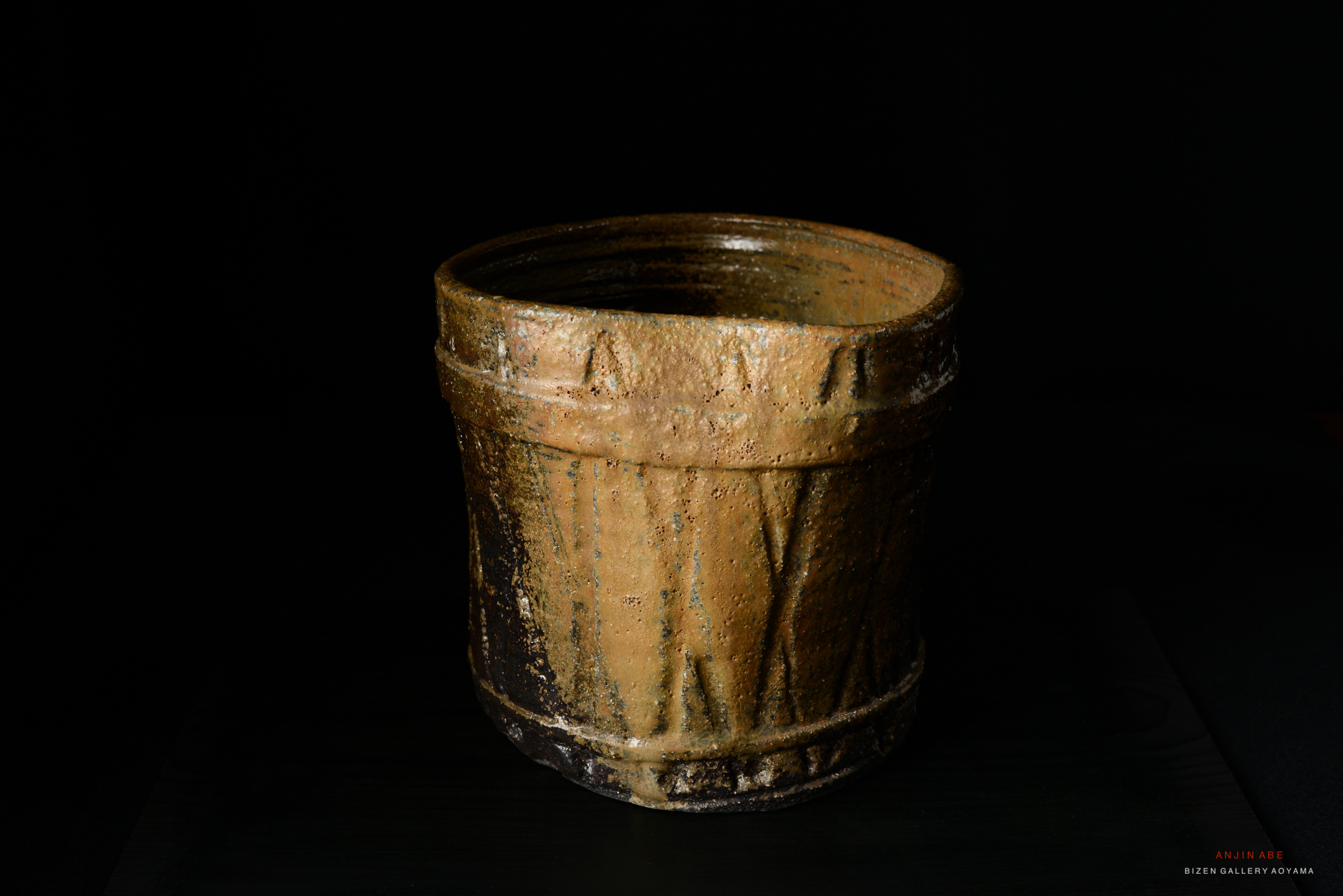 A handcrafted ceramic Mizusashi, showcasing a rustic, textured surface with earthy tones and an organic design, placed against a dark background.