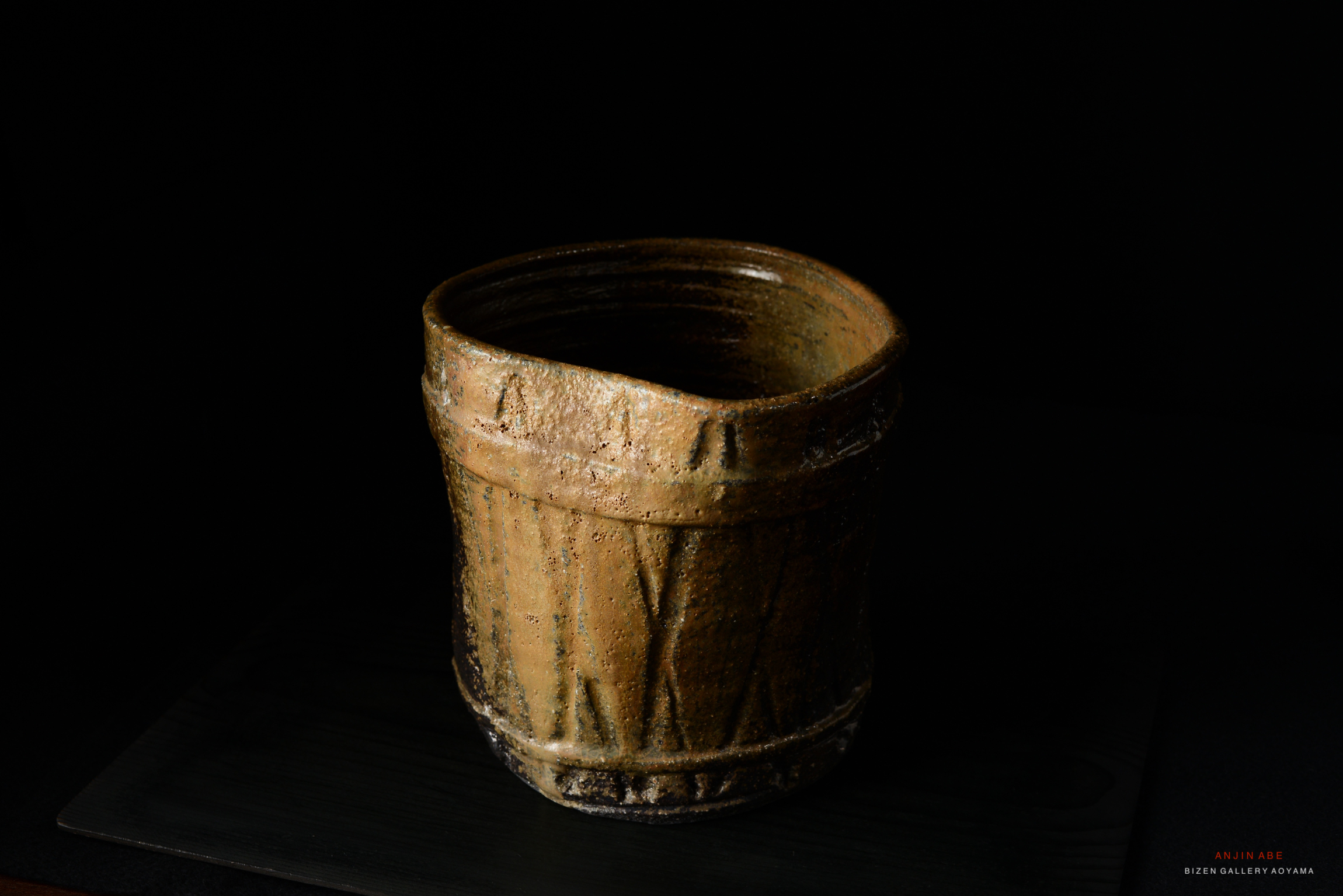 A rustic, handmade ceramic mizusashi (water container) with a textured surface and a slightly irregular shape, set against a black background.