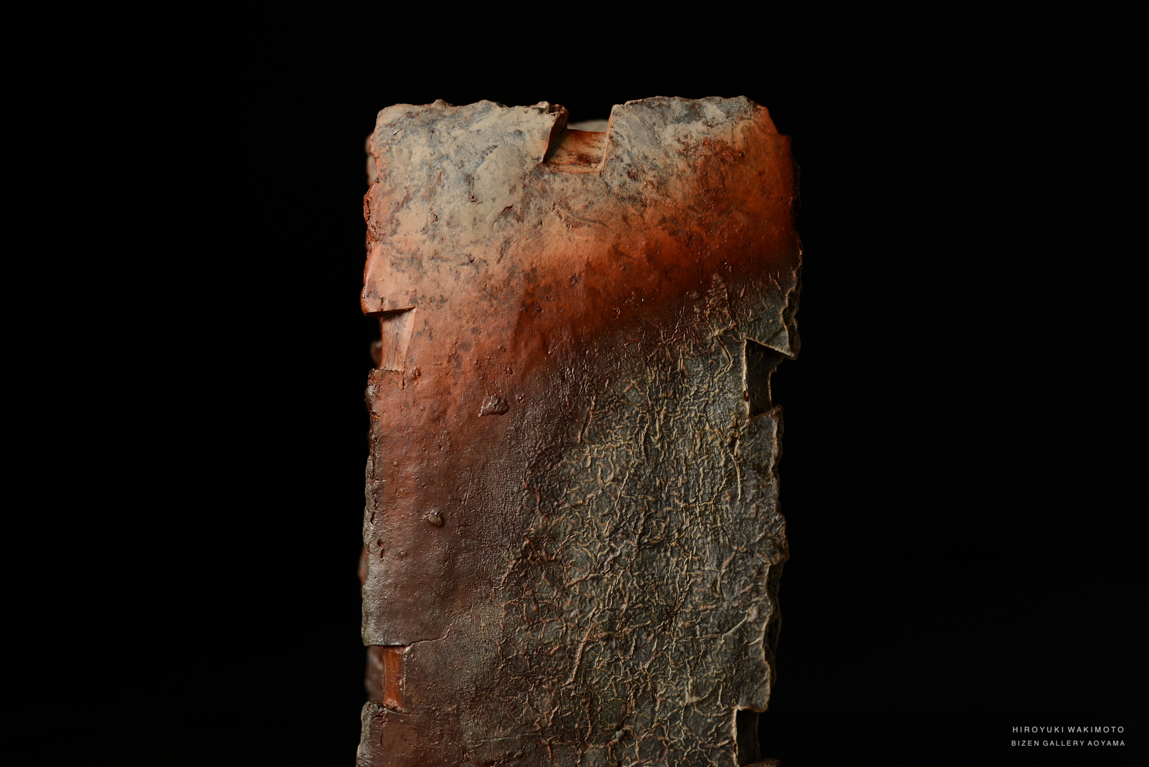 A textured, rustic piece of pottery with a reddish and earthy tone, displayed against a black background.