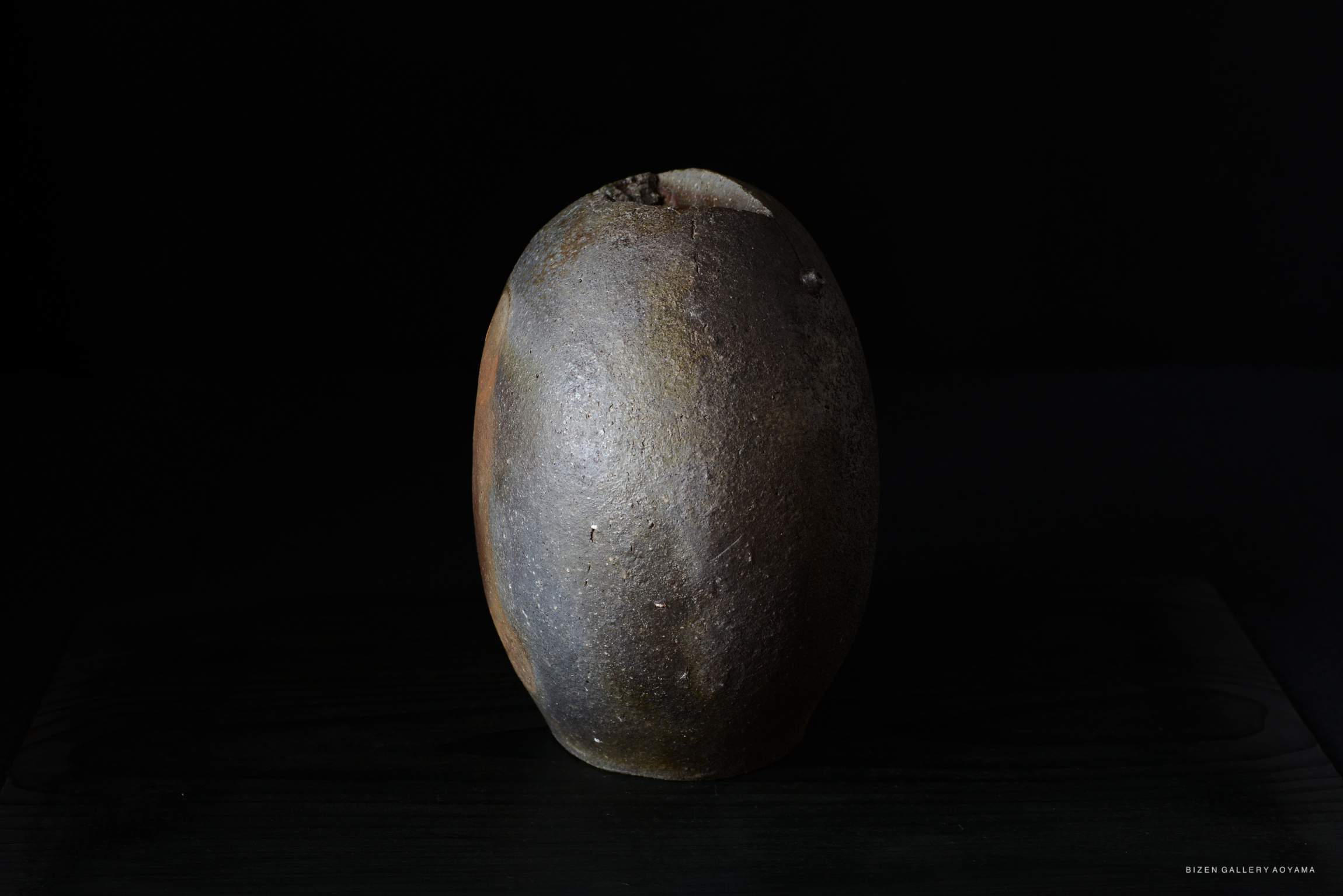 A round, textured clay vase with an earthy color palette, displayed against a black background.